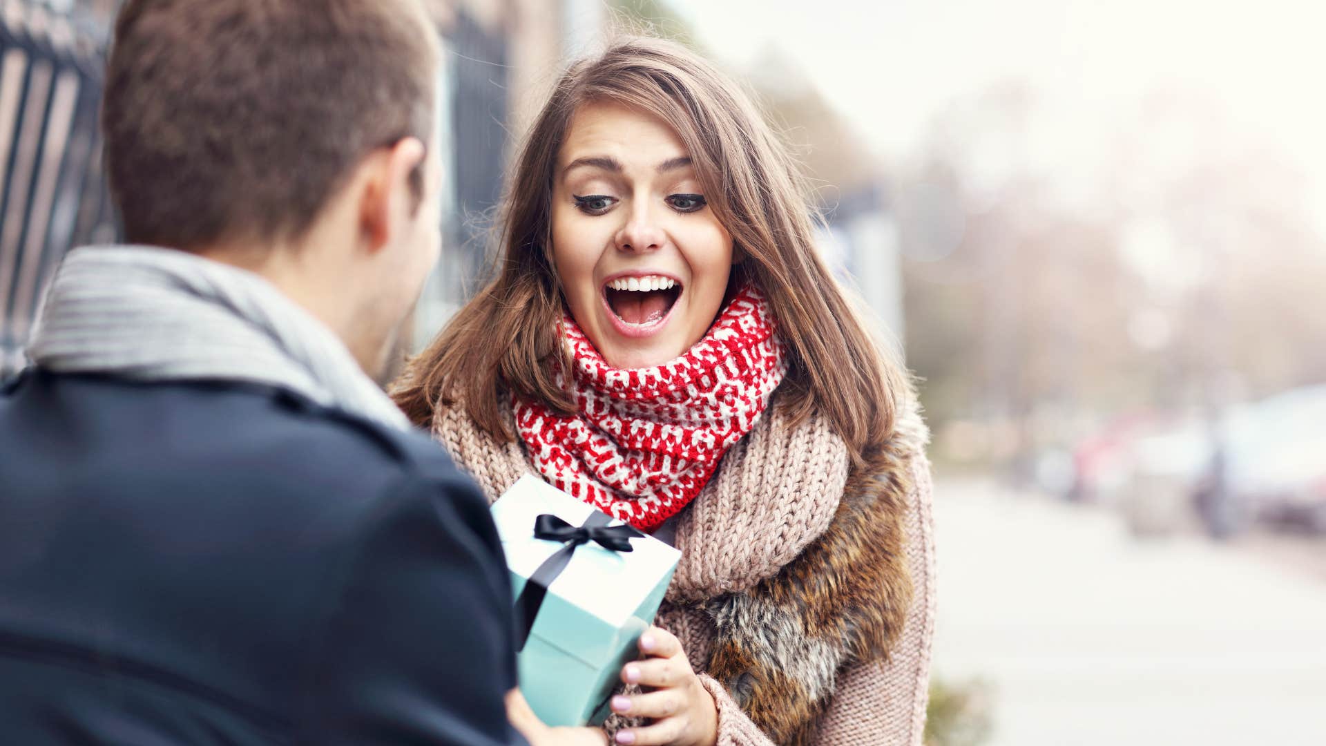 man giving one sided effort to woman in scarf and sweater as she smiles