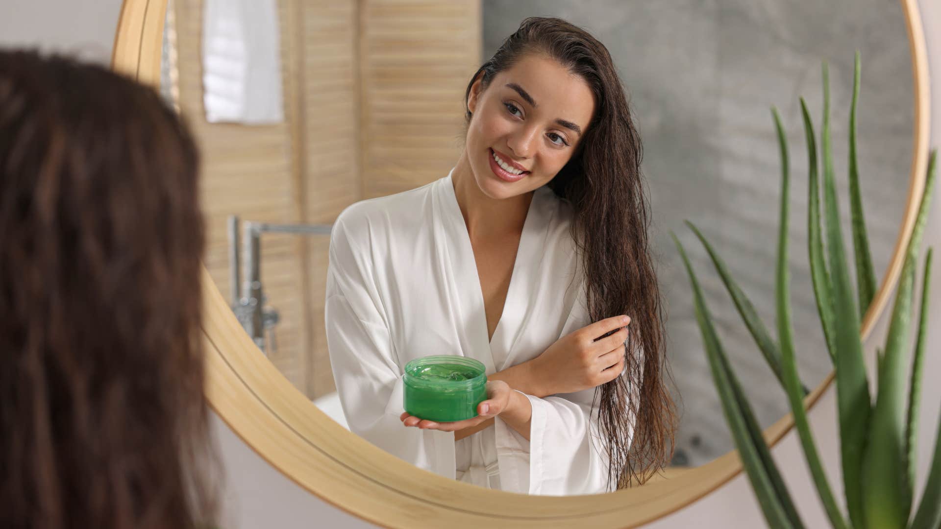 woman with white bathrob putting on diy hair mask while smiling at mirror