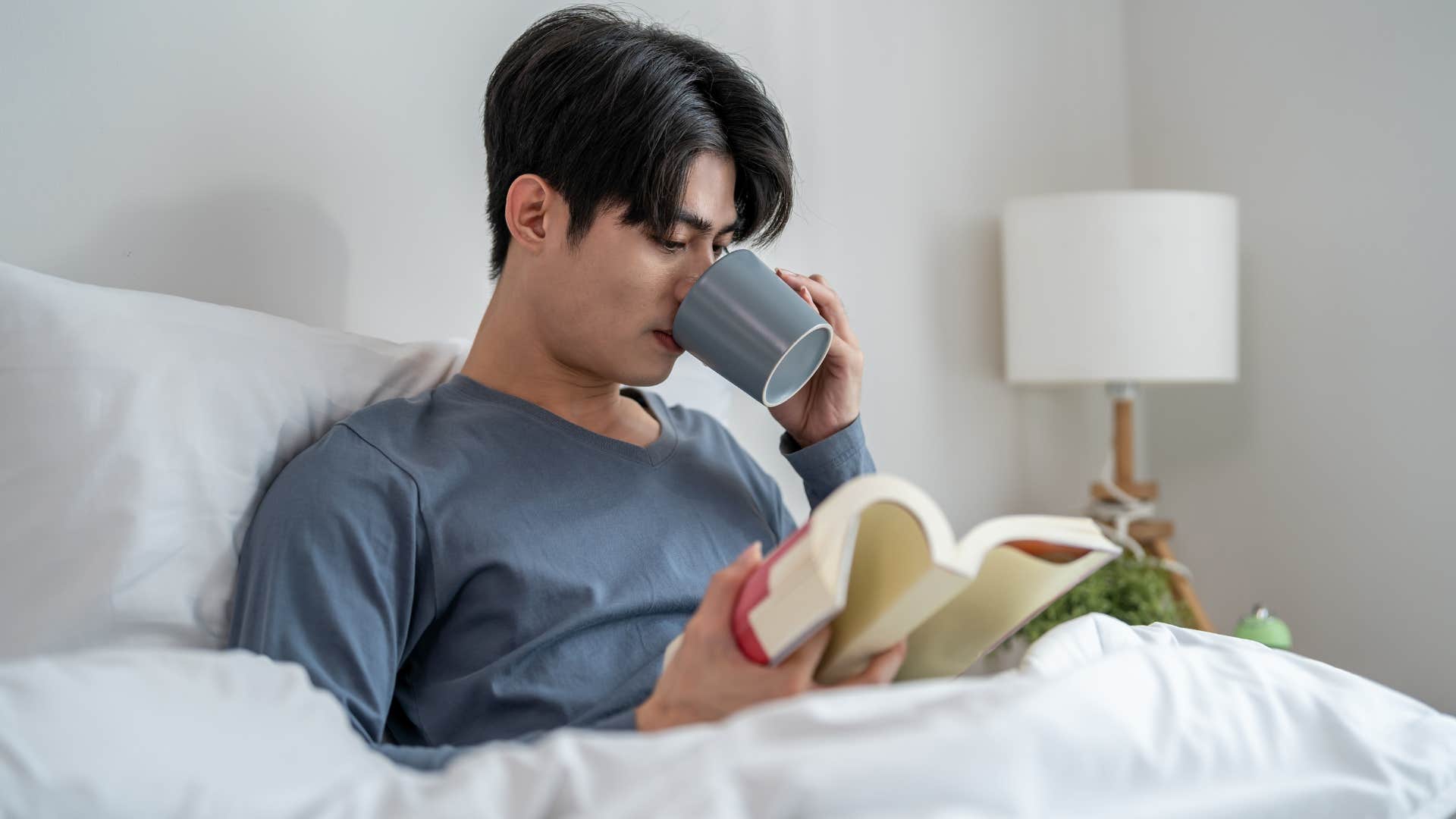 man in gray shirt getting up early in the morning to be productive as he reads book and sips tea