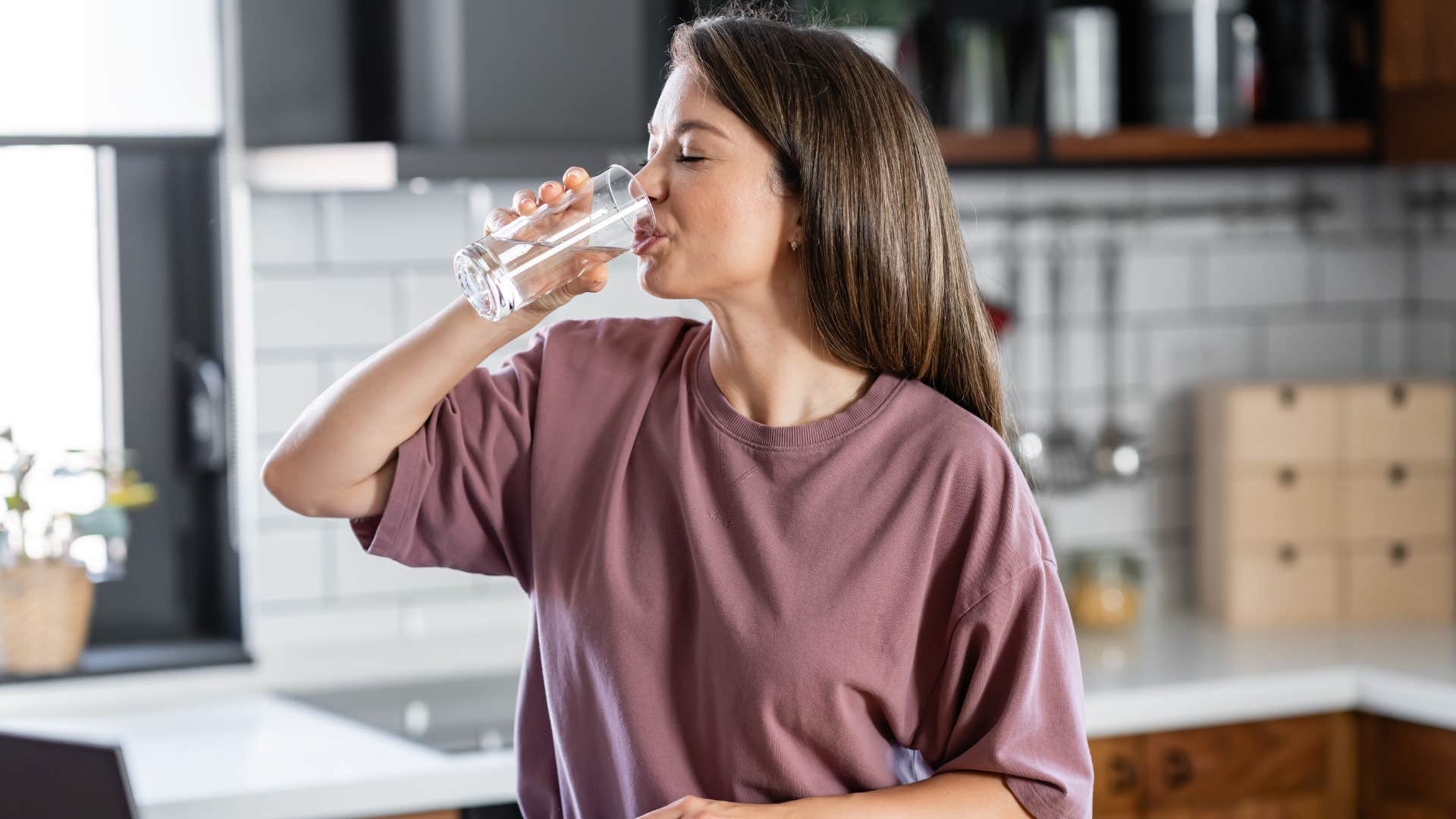 woman in blush shirt drinking water as she does intermittent fasting 