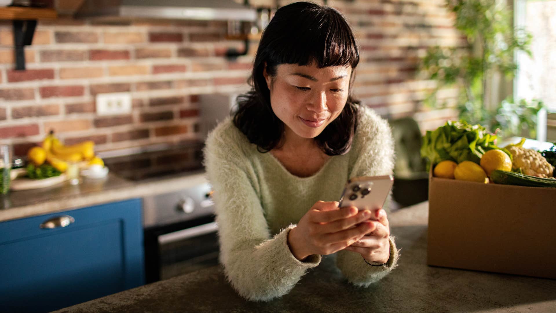 woman in green shirt meal prepping for the week as she looks at phone