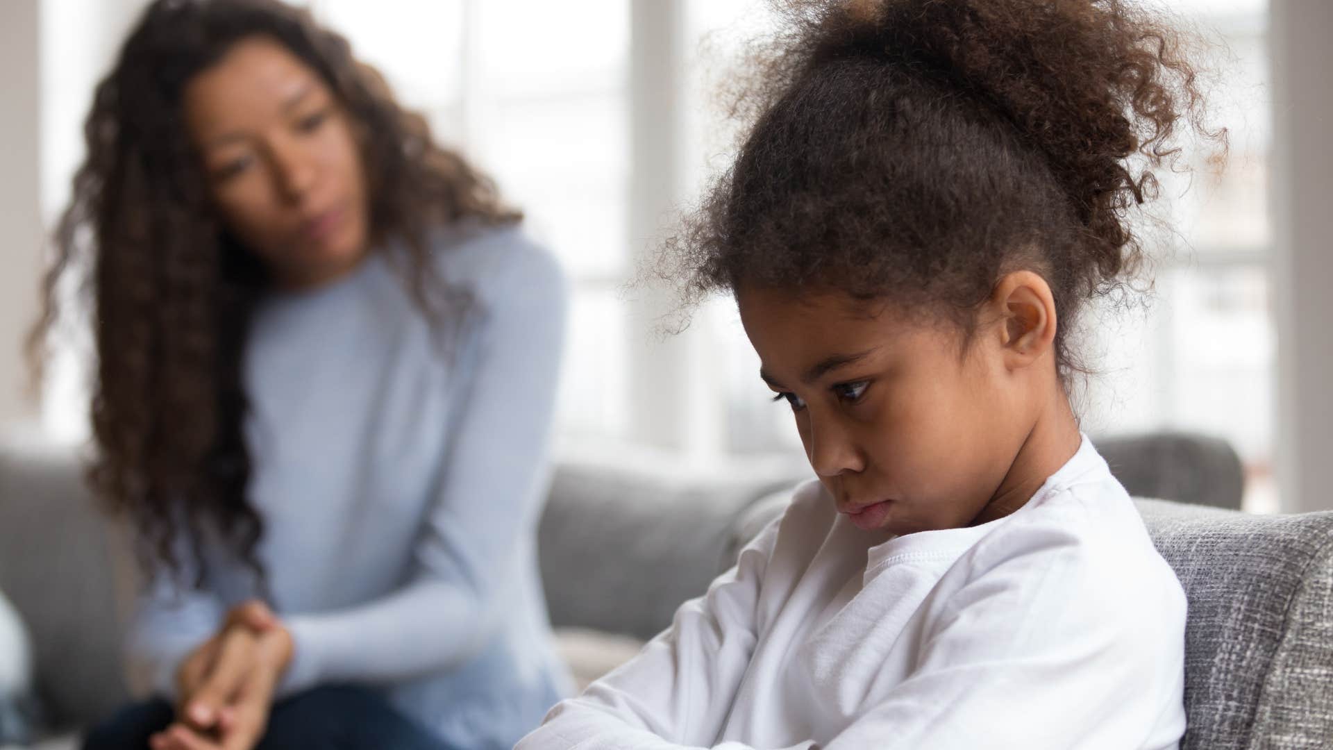 little girl having temper tantrum sitting beside mom on couch