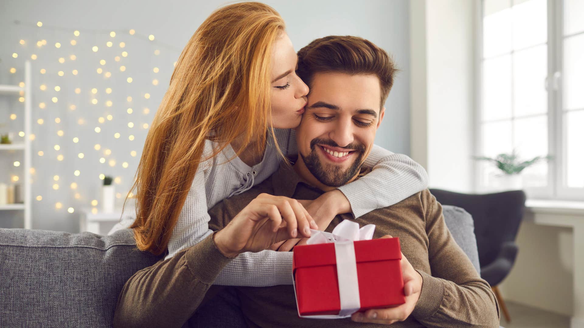 woman surprising man with thoughtful gifts as she gives him red box