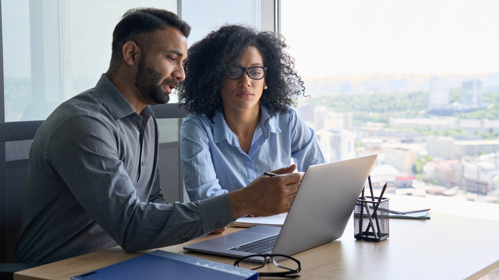 man showing woman a simpler way to do something as they work on laptop
