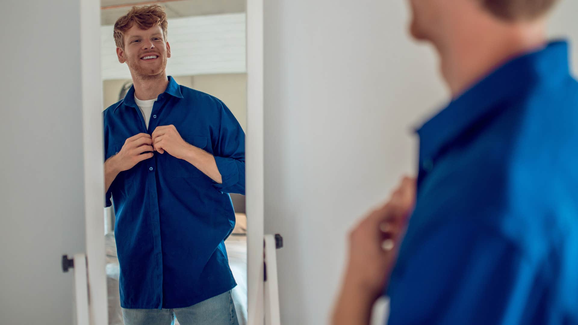 man looking in the mirror smiling trying on clothes