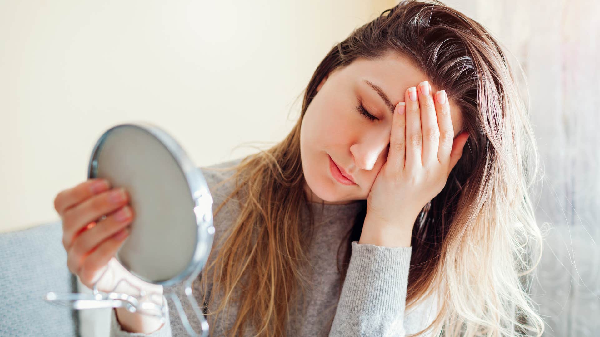 stressed woman with greasy hair looking in a mirror