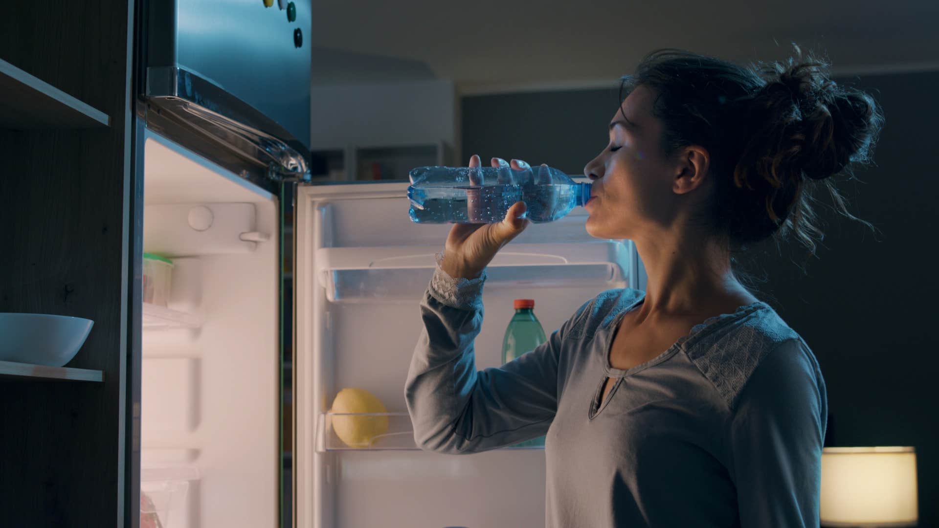 woman drinking bottle of water from fridge