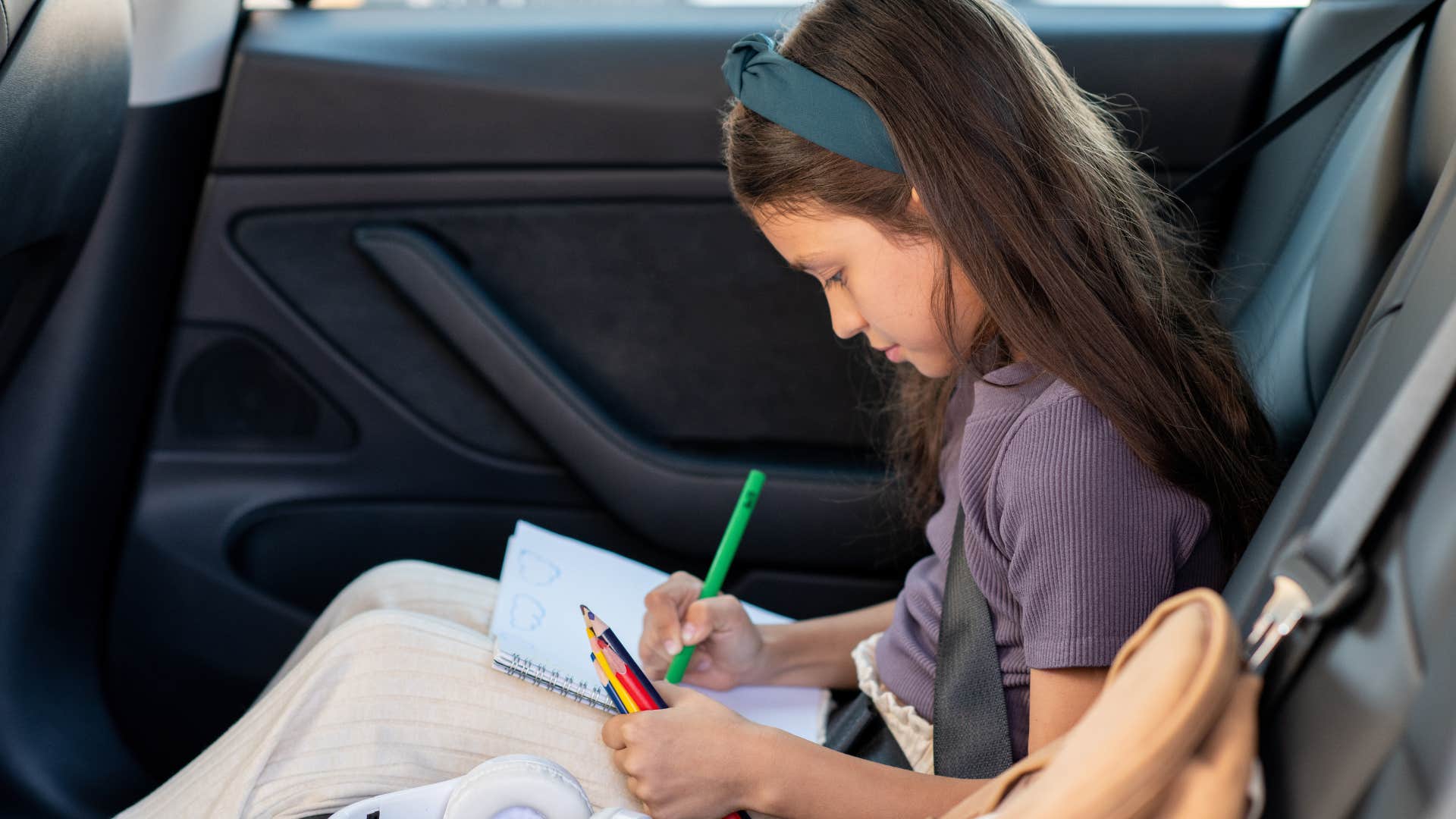 little girl drawing with crayons in backseat of car