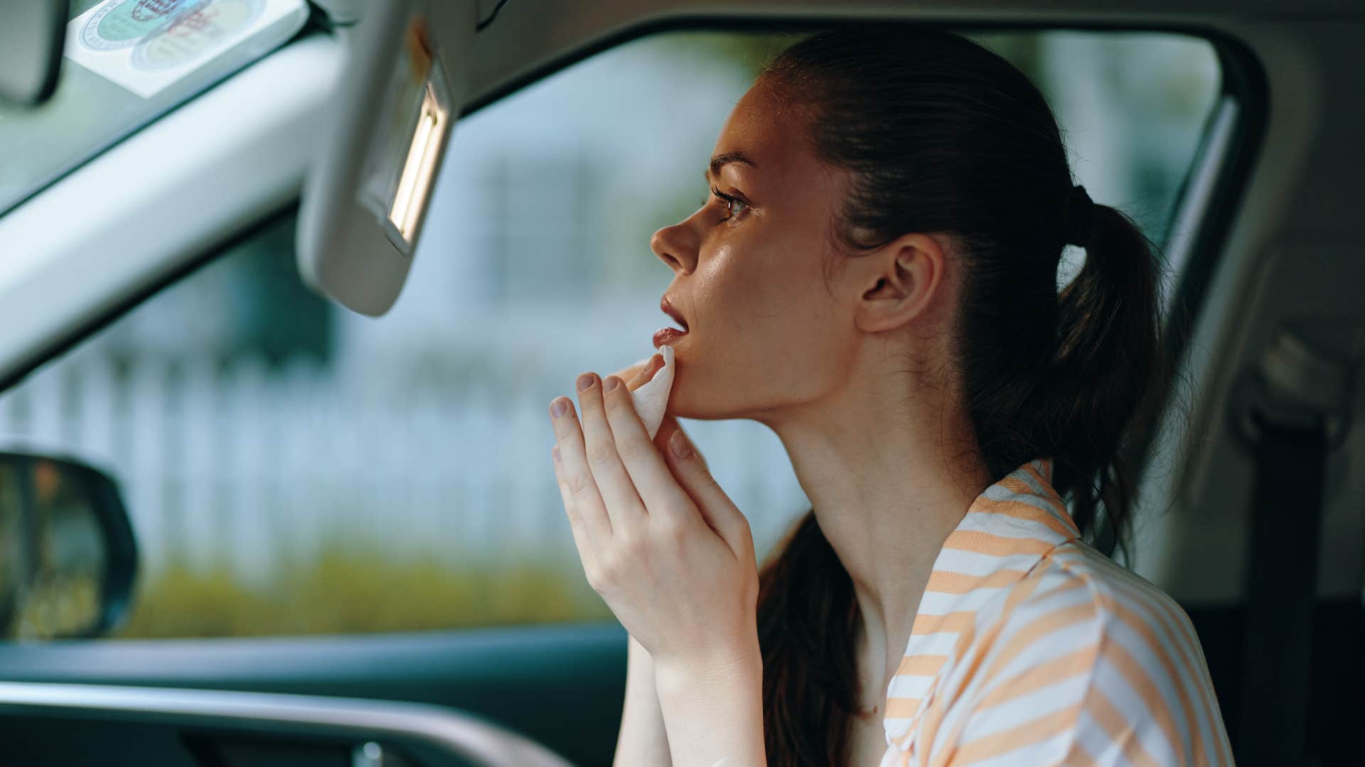 woman putting on sunscreen in her car mirror