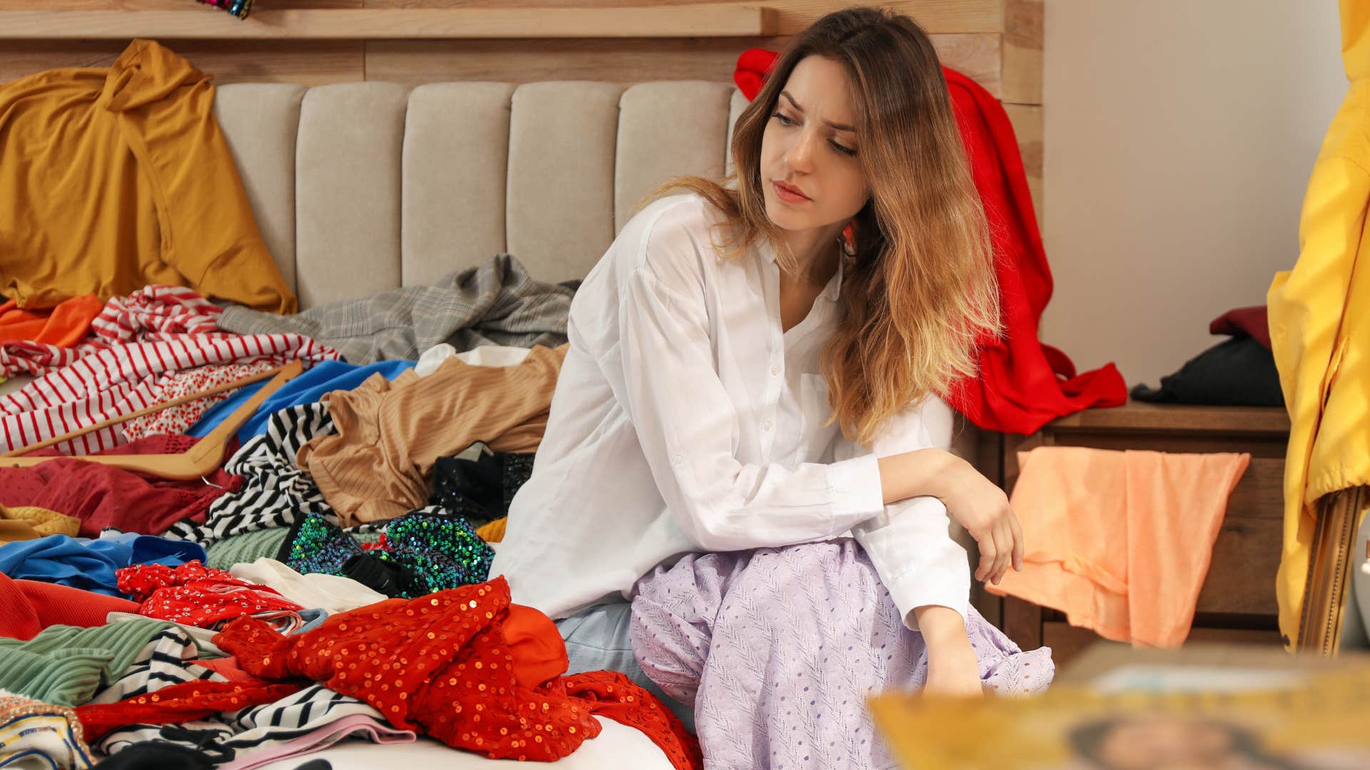 Woman sitting on her bed with clutter everywhere.