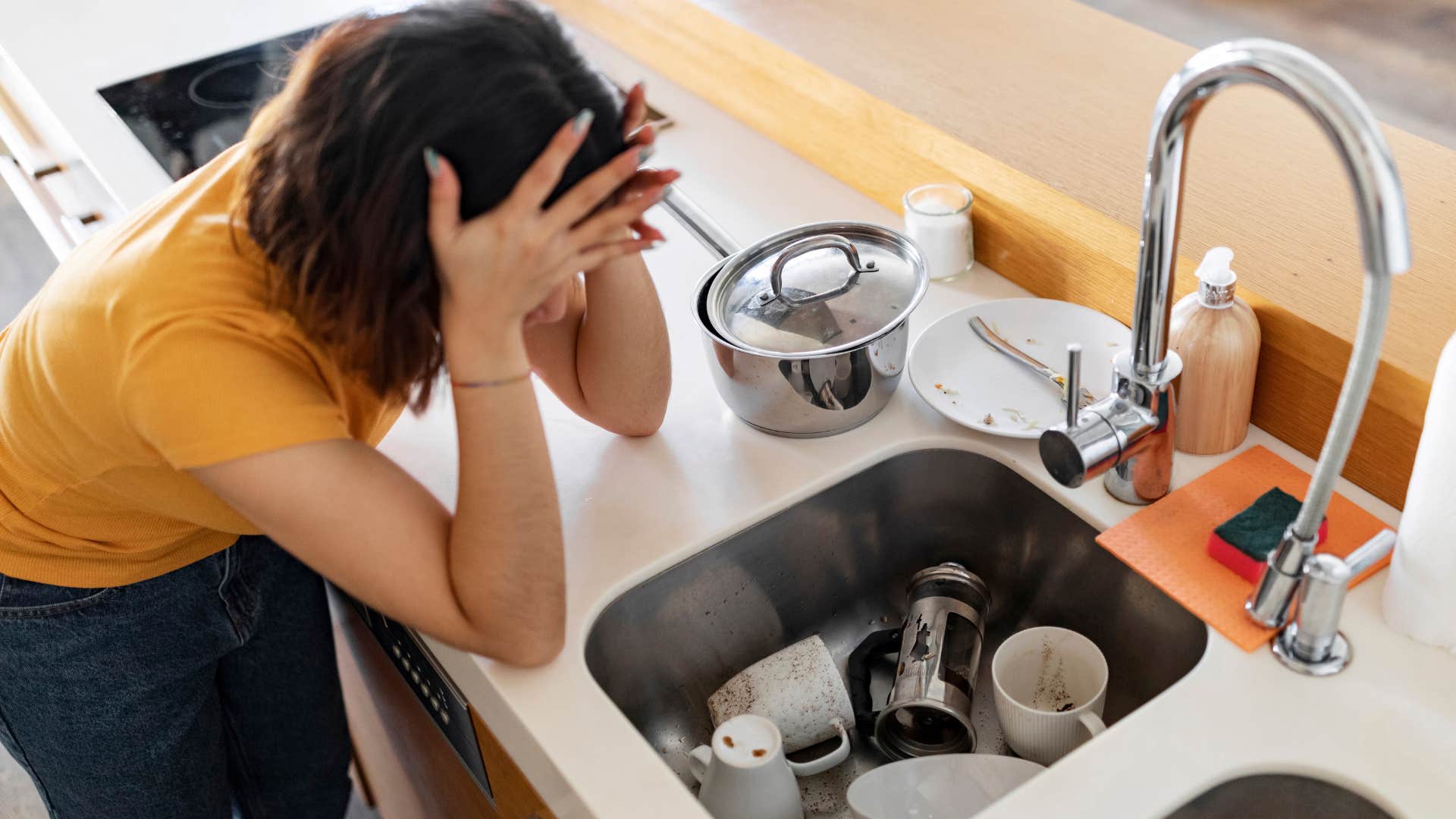 Woman holding her head with dirty dishes scattered around at her house.