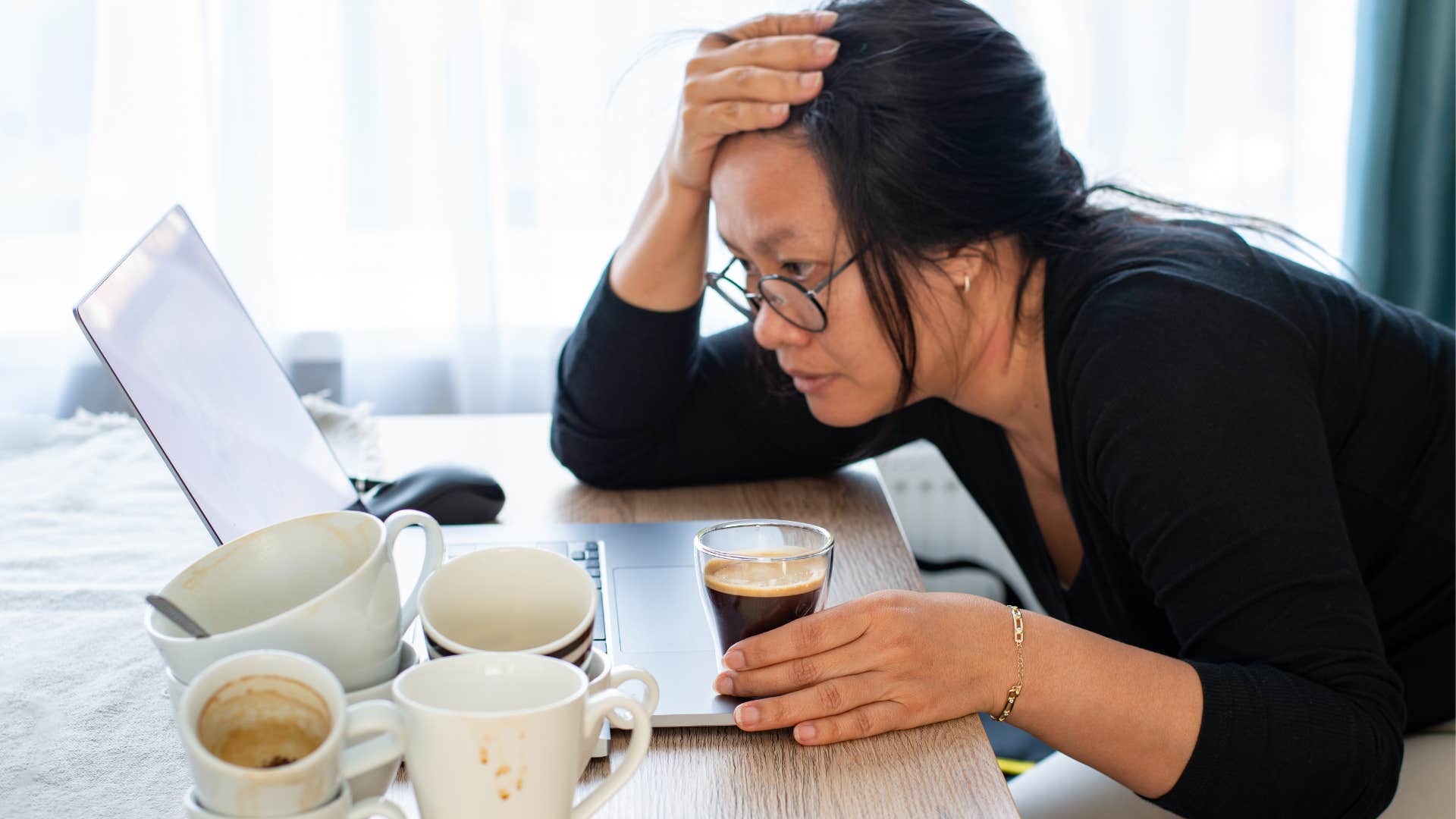 Woman surrounded by multiple coffee cups at home.
