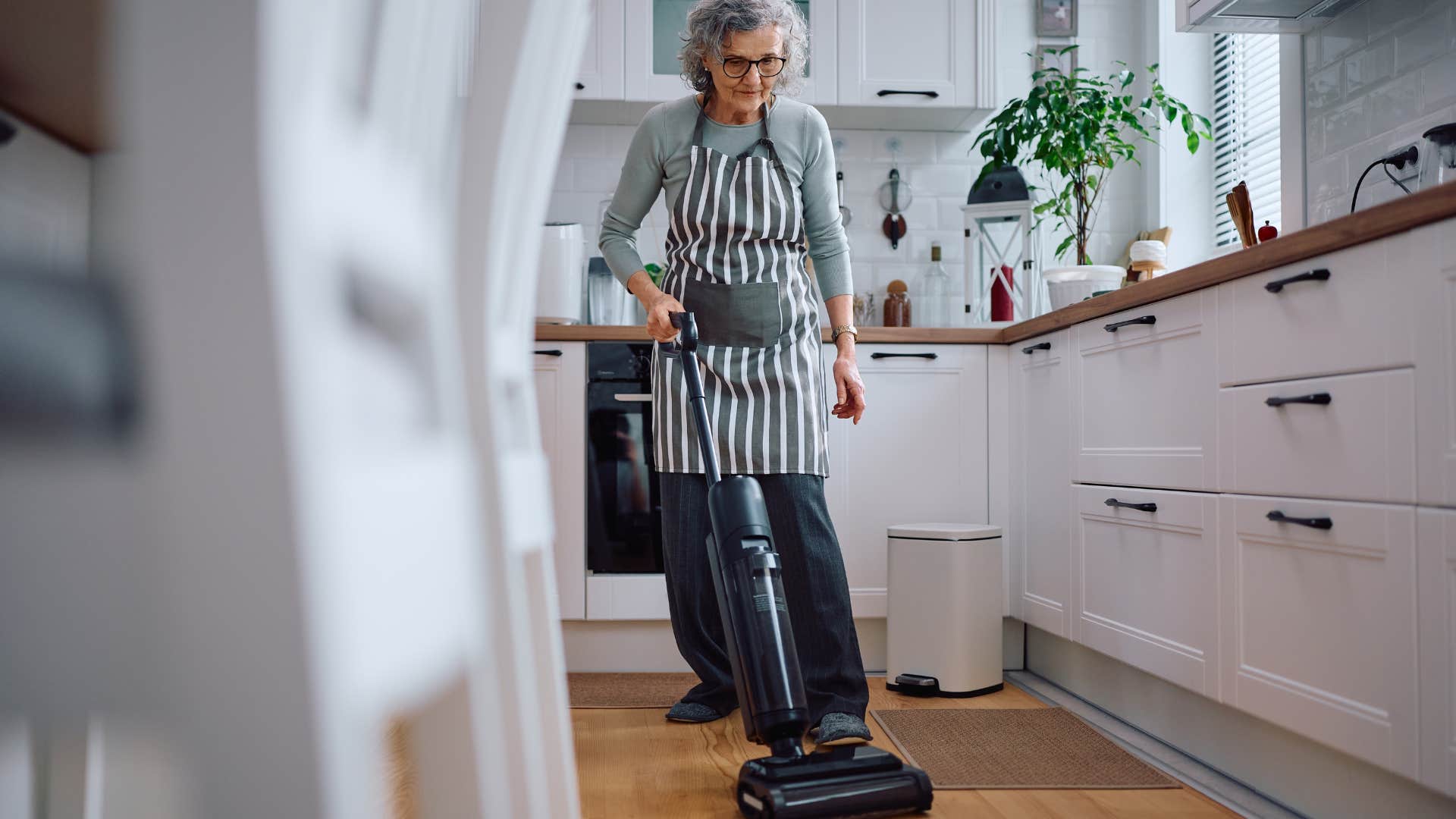 older woman vacuuming floor in kitchen