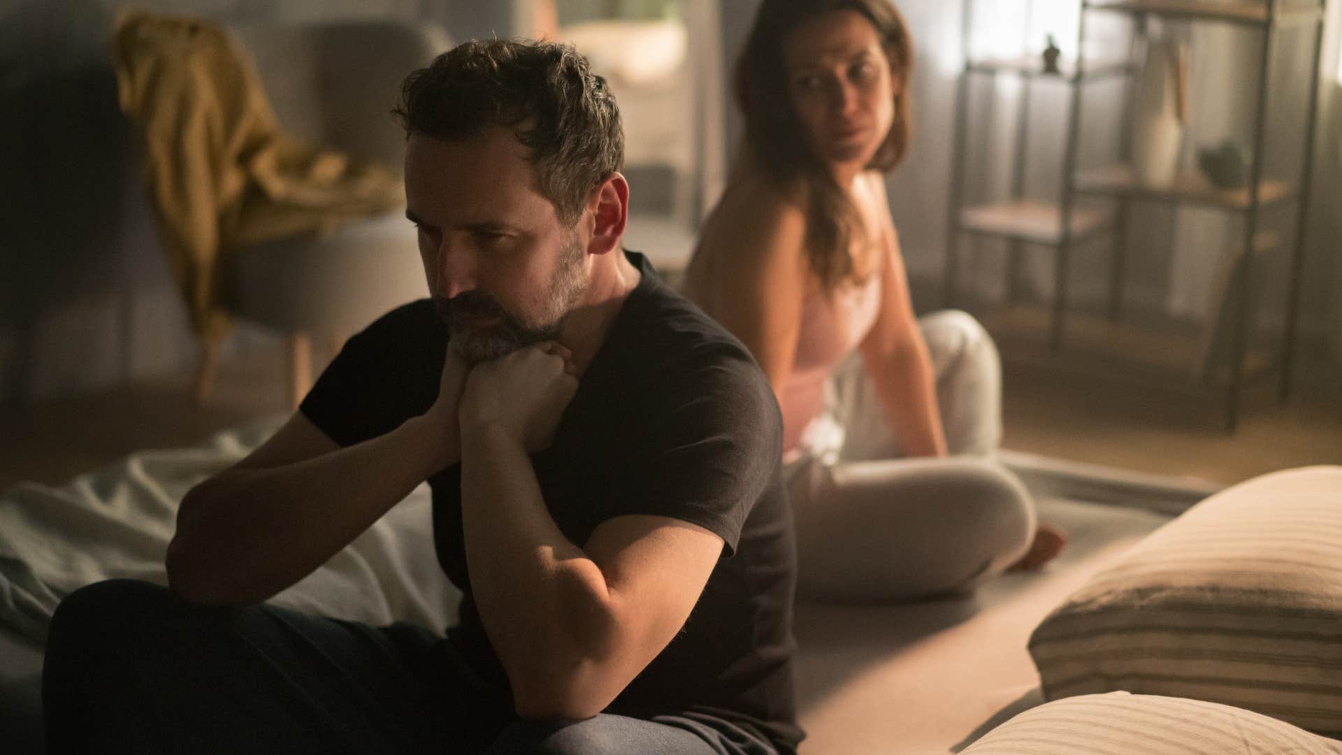 upset man sitting away from significant other on bed