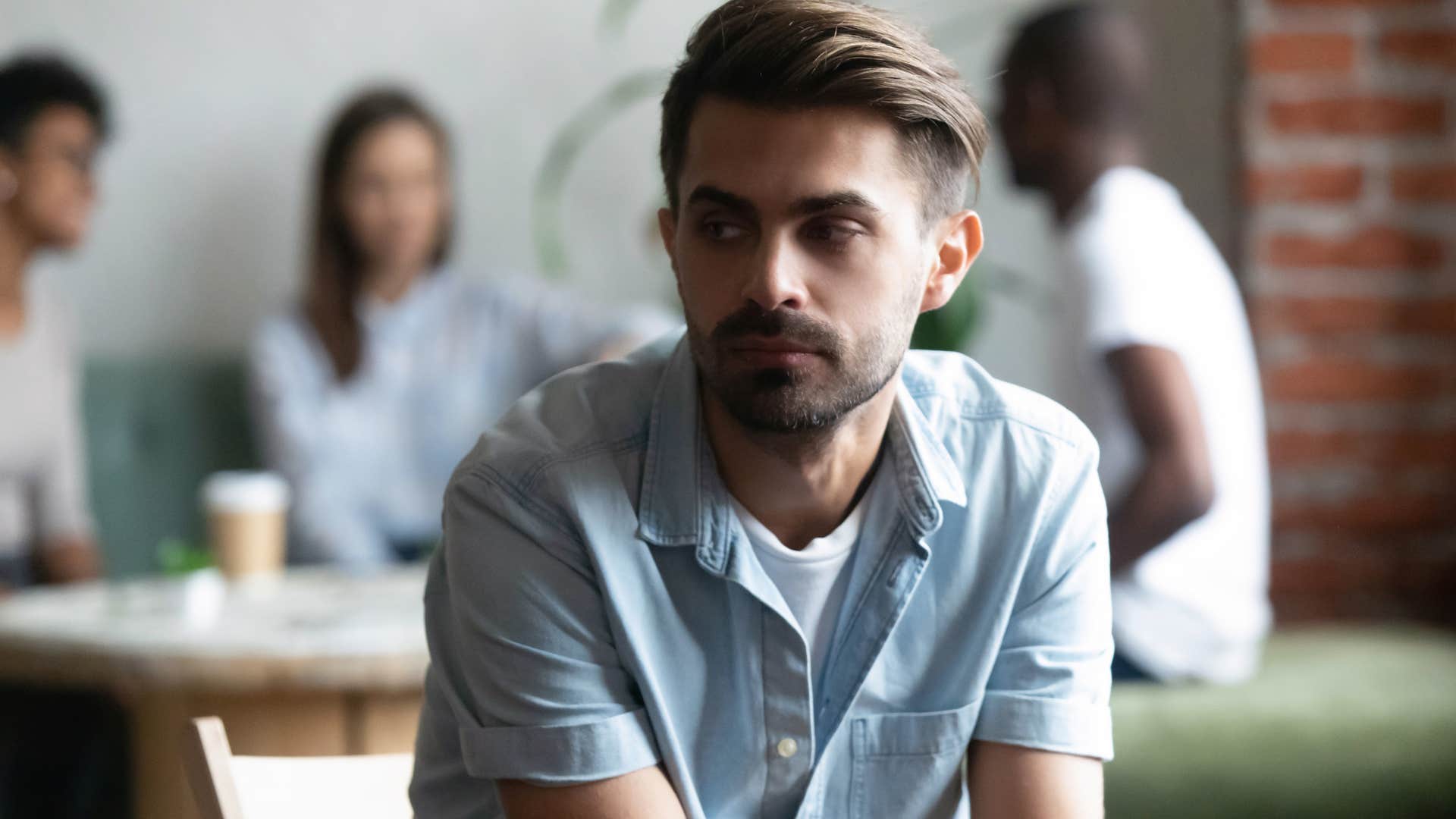 man sitting with physical space between him and his friends