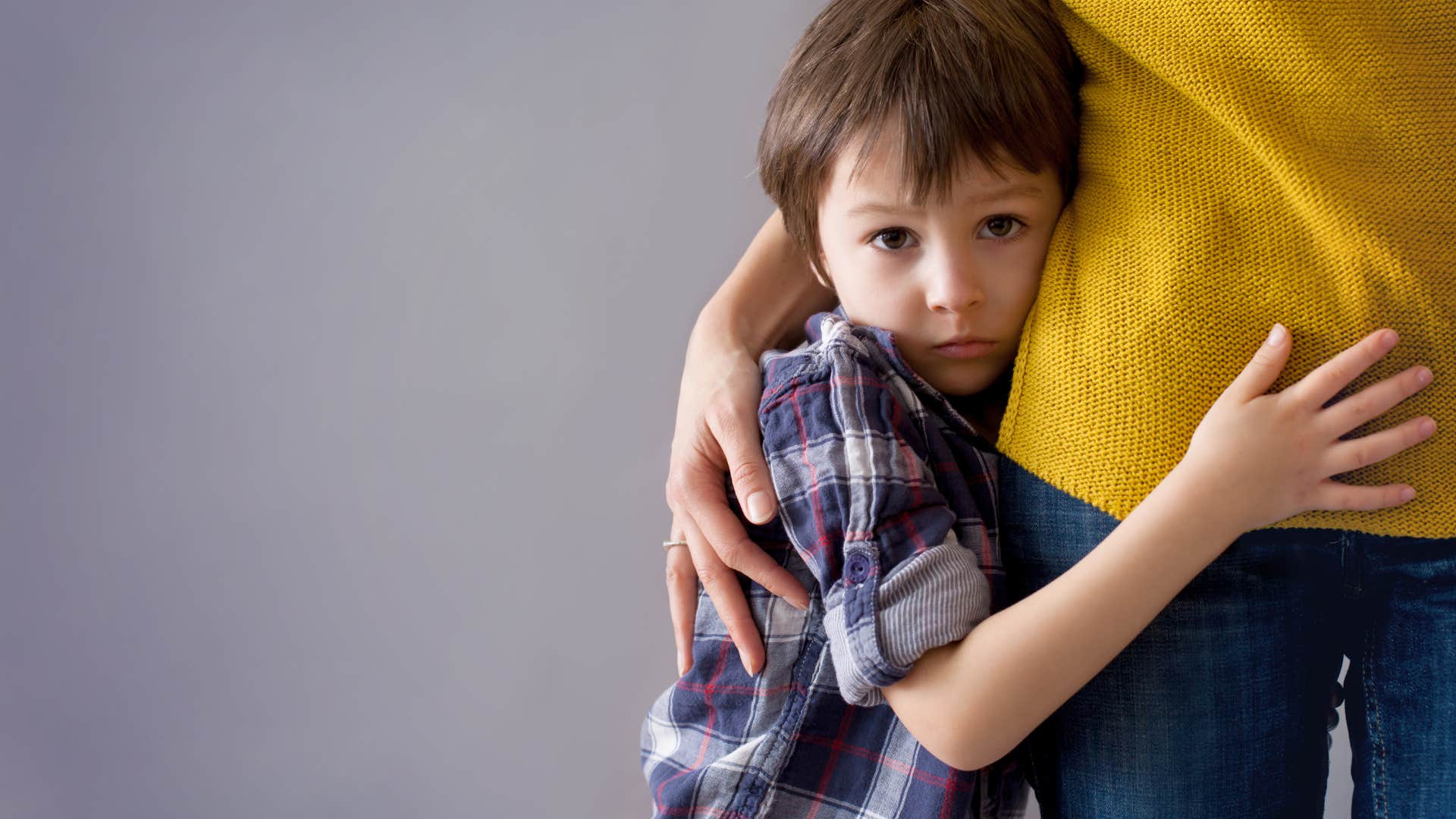 child clinging to the leg of their parent