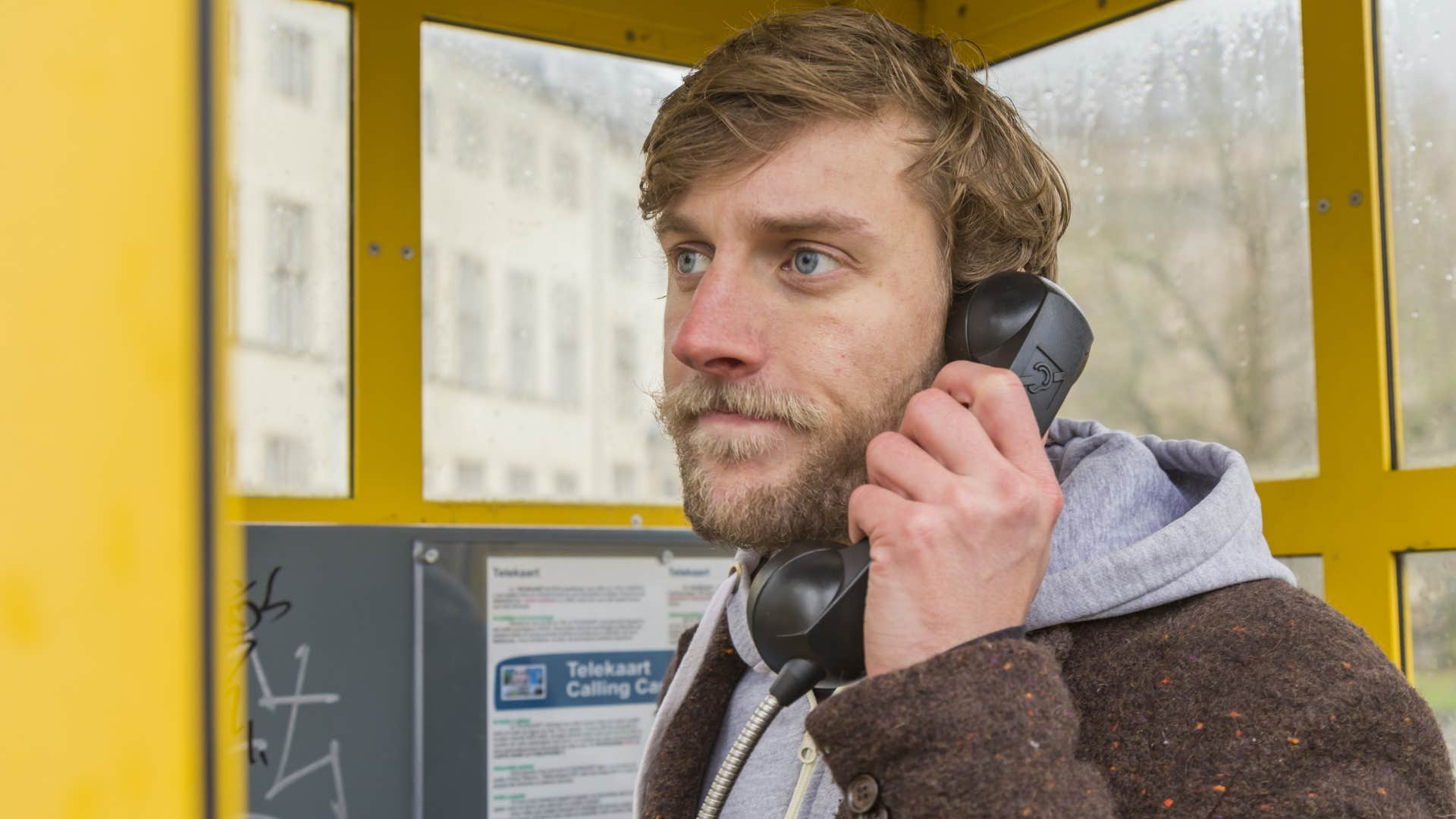 man in brown jacket answering phone mounted to booth