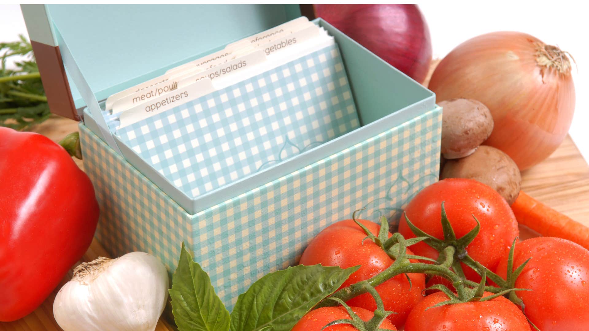 a blue recipe box stuffed with handwritten cards surrounded by vegetables