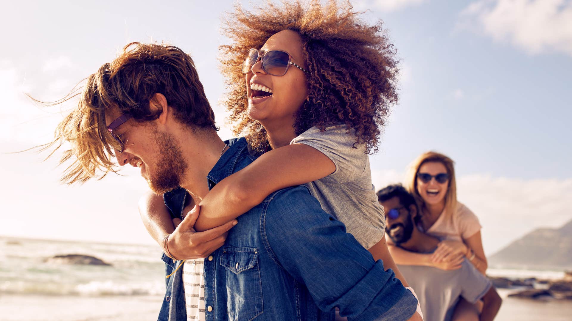 extroverted couples piggyback on a beach in warm weather