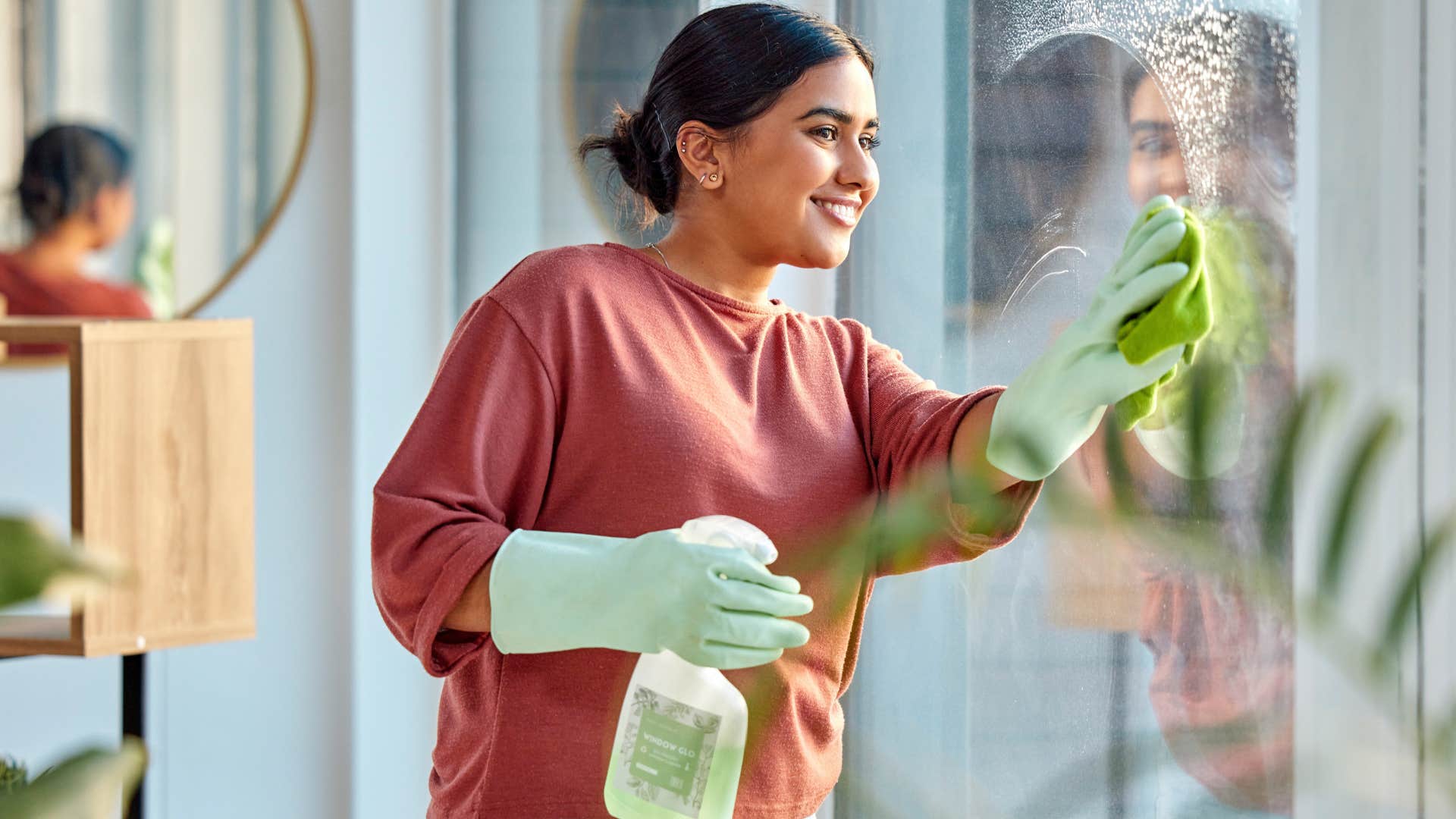 Woman with clean spaces washing windows and smiling.