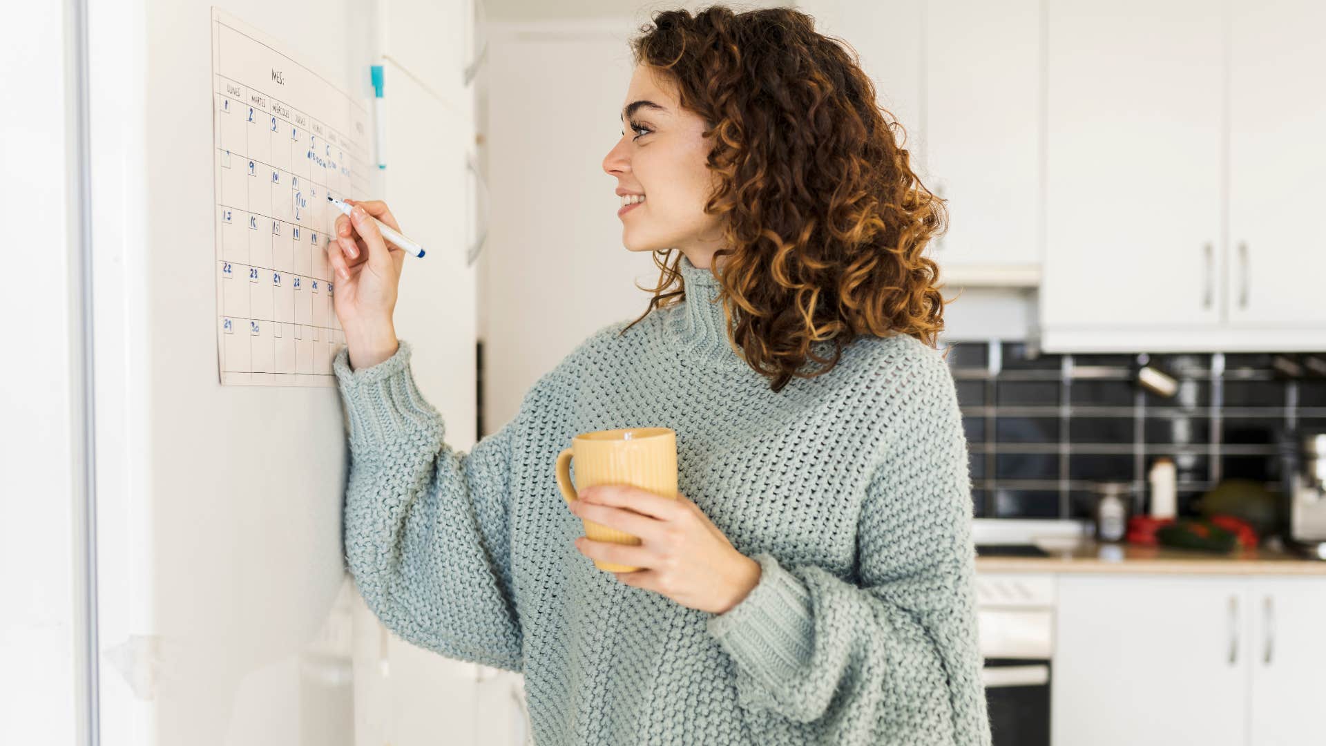 Woman smiling and writing in her personal calendar at home.
