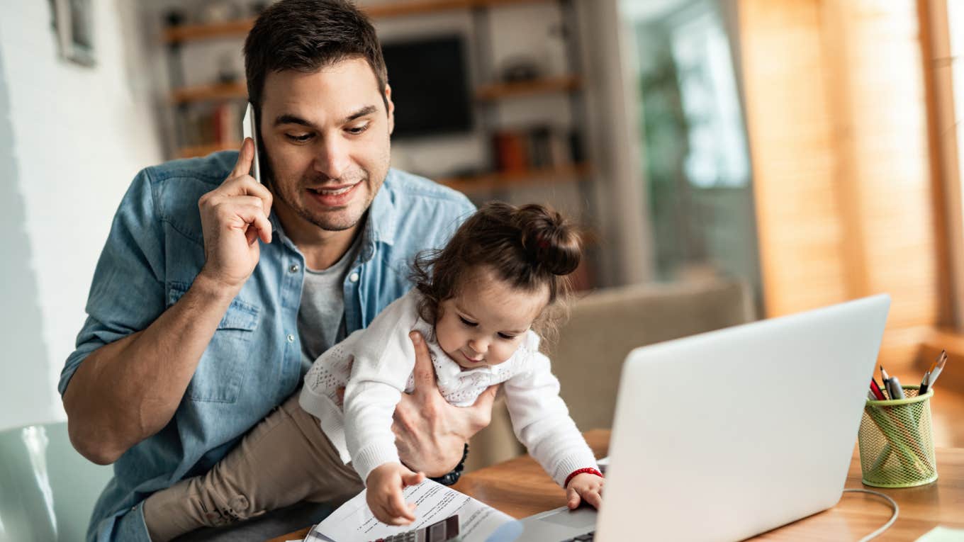 dad working on laptop and holding infant daughter