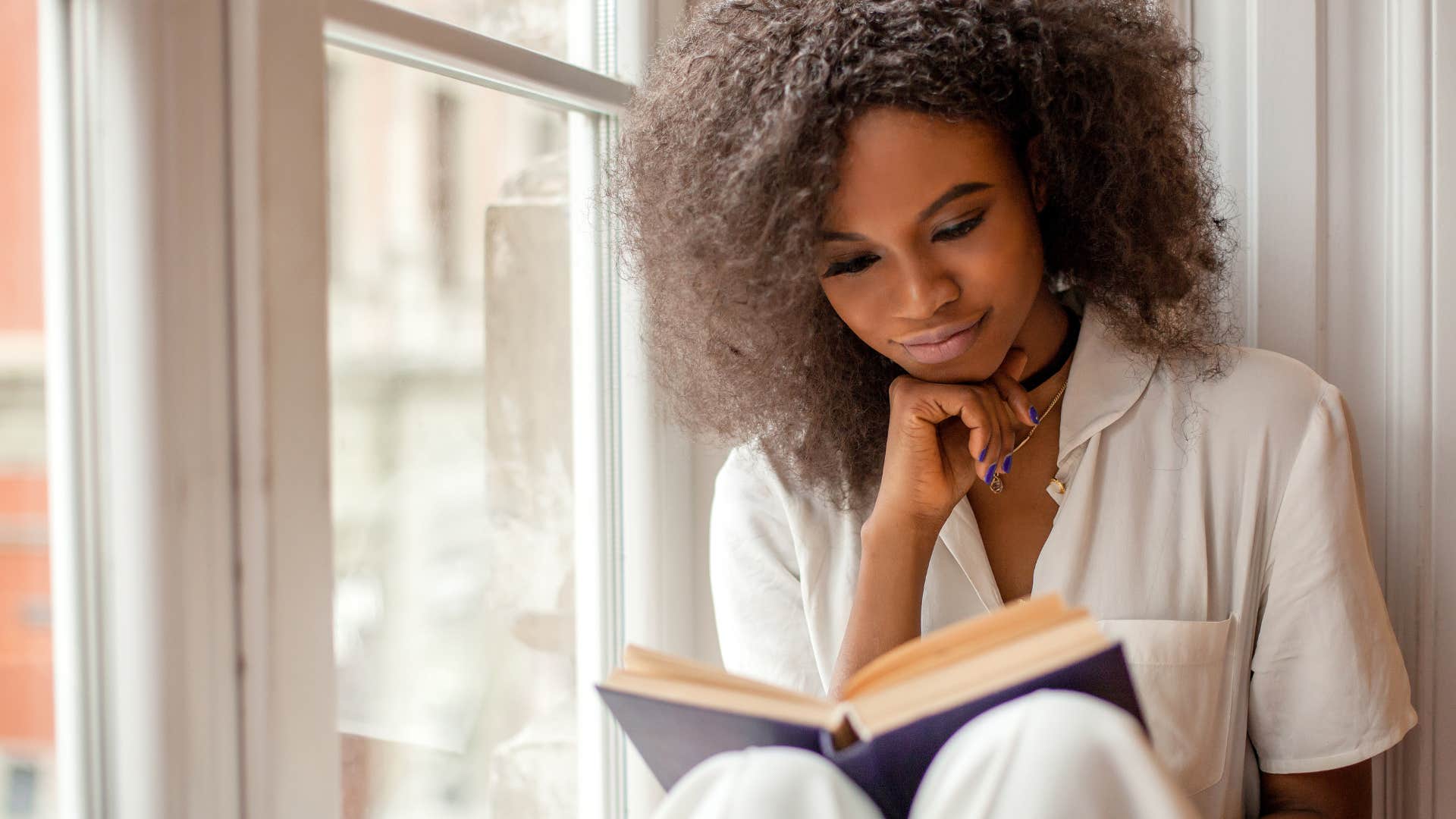 woman reading book in windowsill to feel inspired