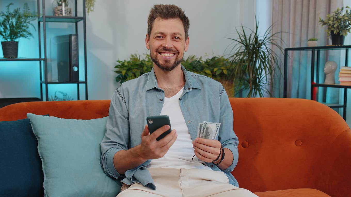 frugal man sitting on his couch holding money