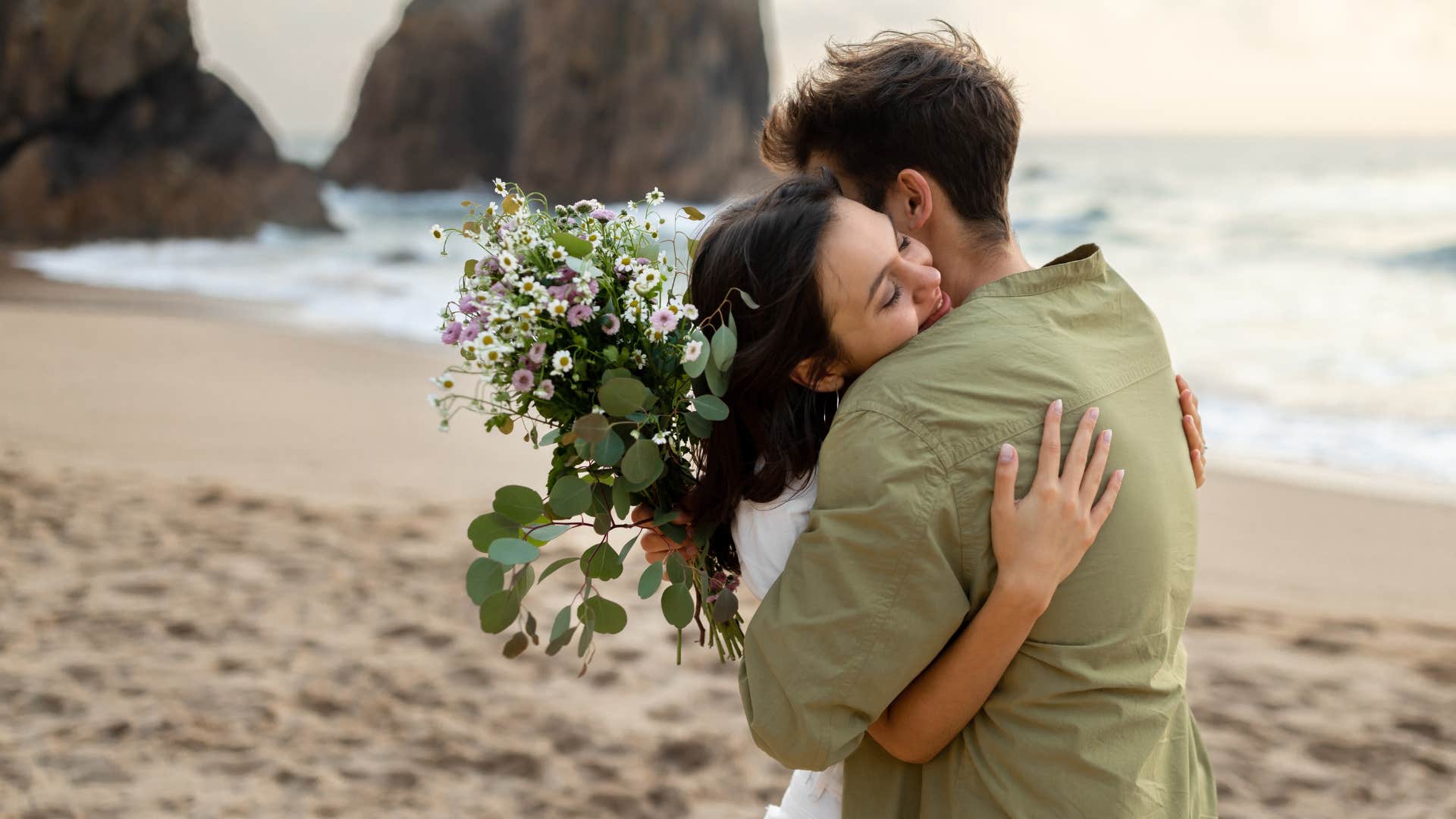 couple hugging as man has flowers in hand