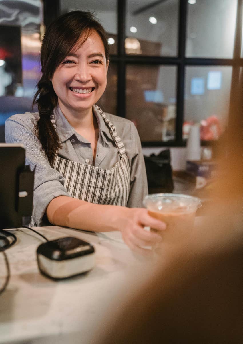 barista handing a coffee to customer who placed an order at a cash register