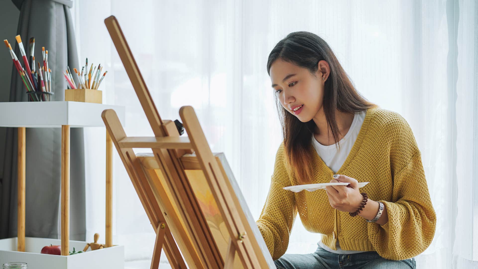 woman in yellow sweater finding ways to turn boredom into creativity as she paints