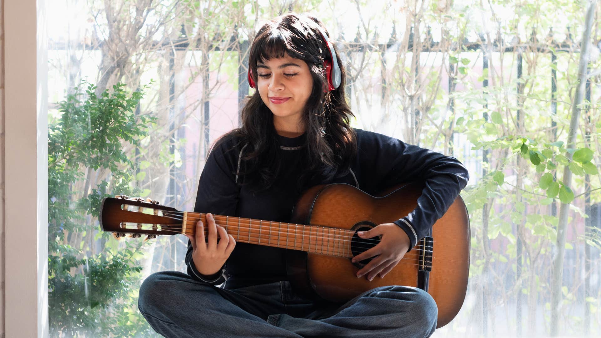 woman in black shirt strumming guitar as she learns skills independently