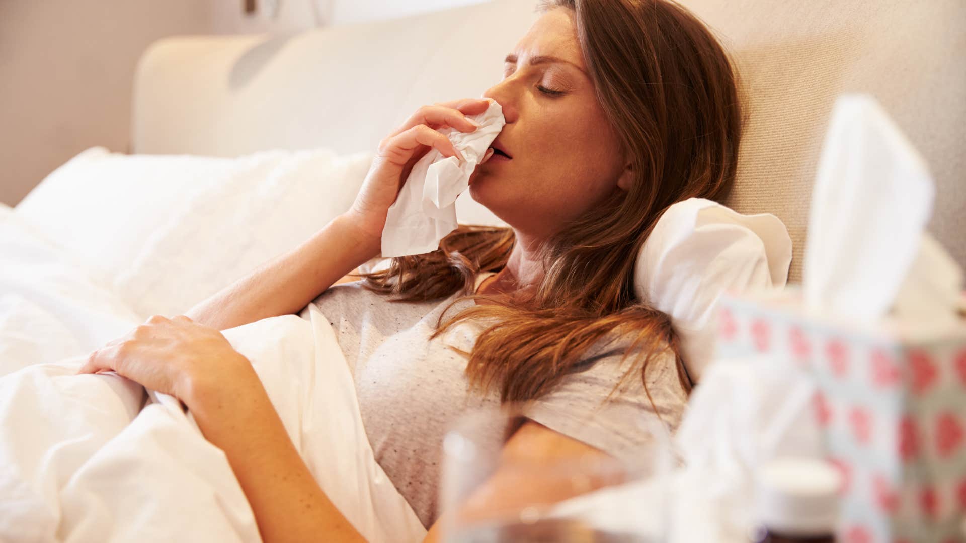 sick woman lying in bed blowing her nose