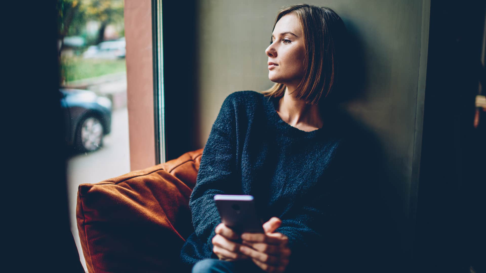 woman sitting on window ledge holding phone
