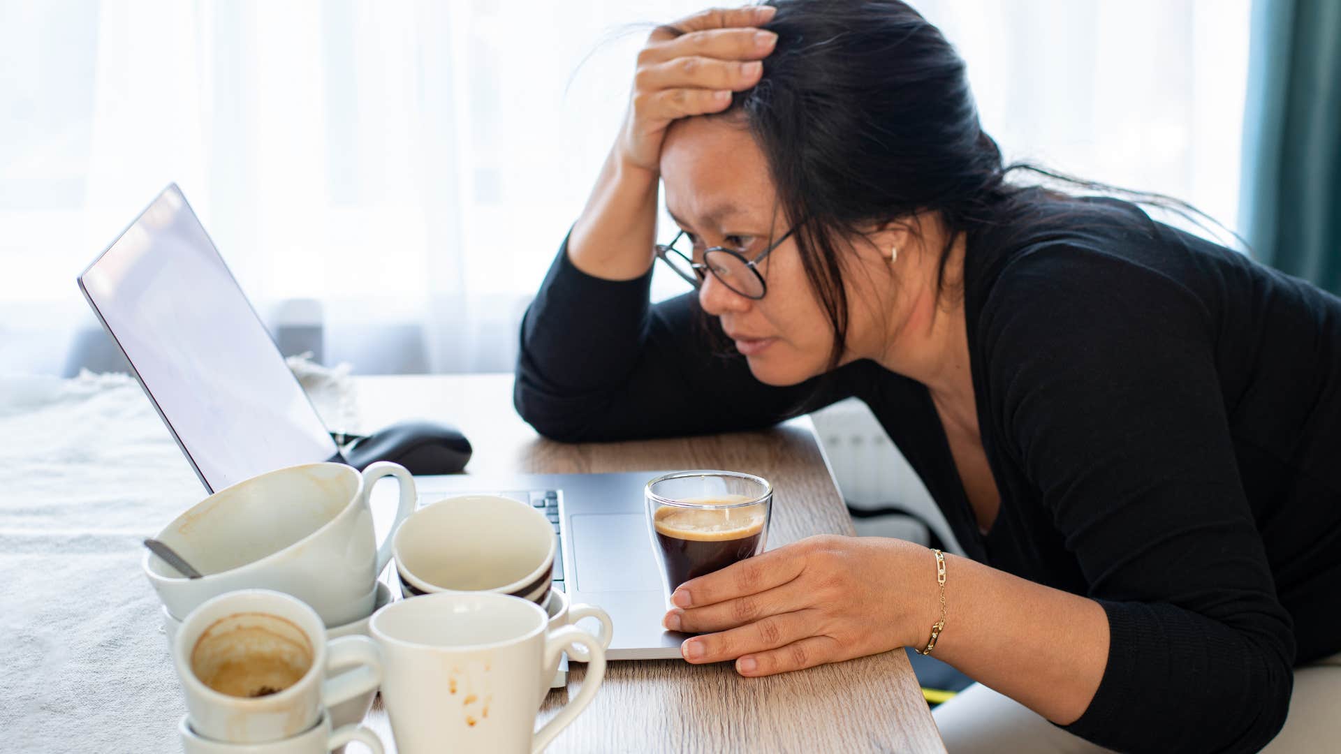 Woman sitting with coffee cups everyone and looking at a laptop.