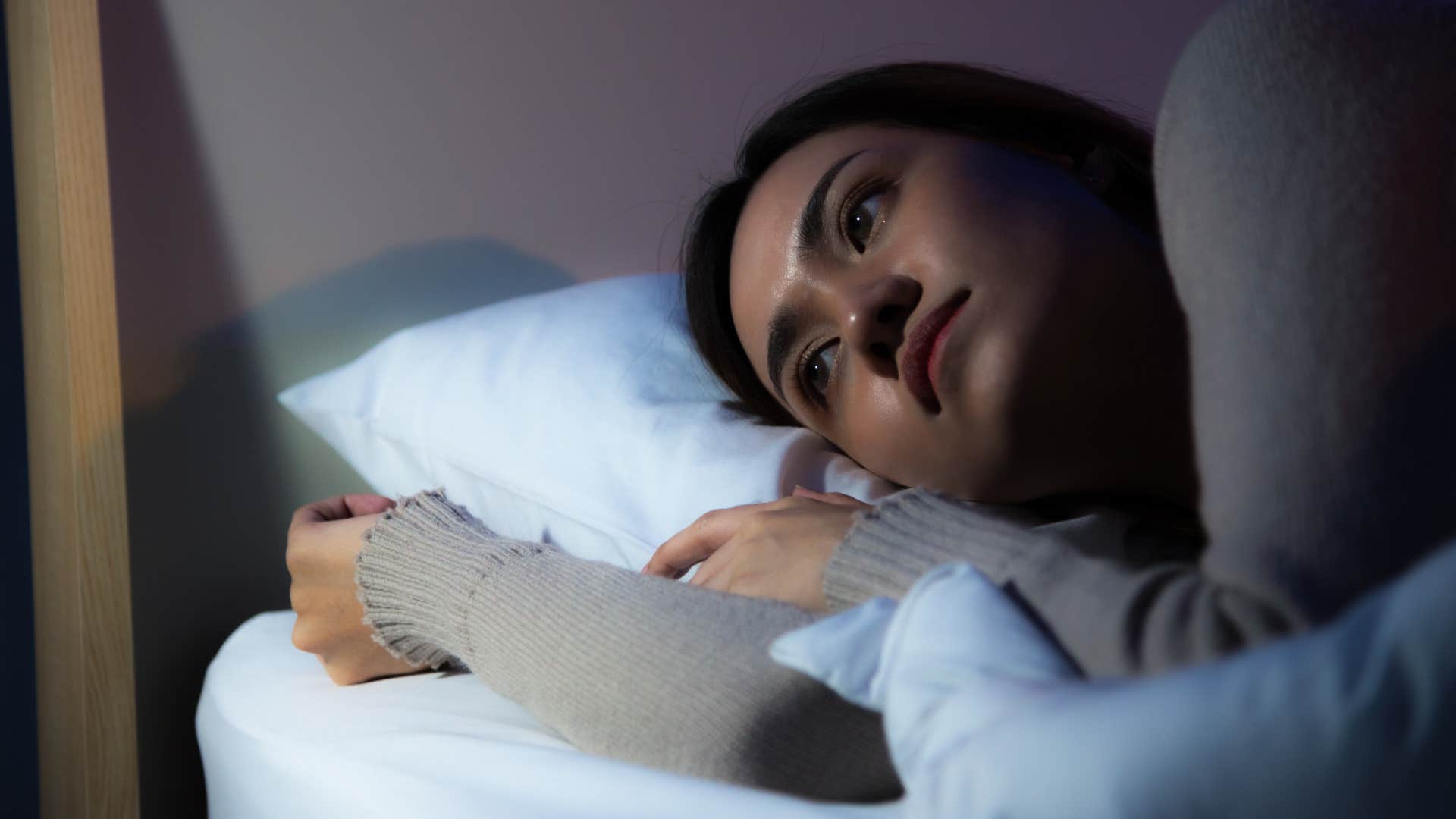 Woman laying awake in her bedroom that is bare.