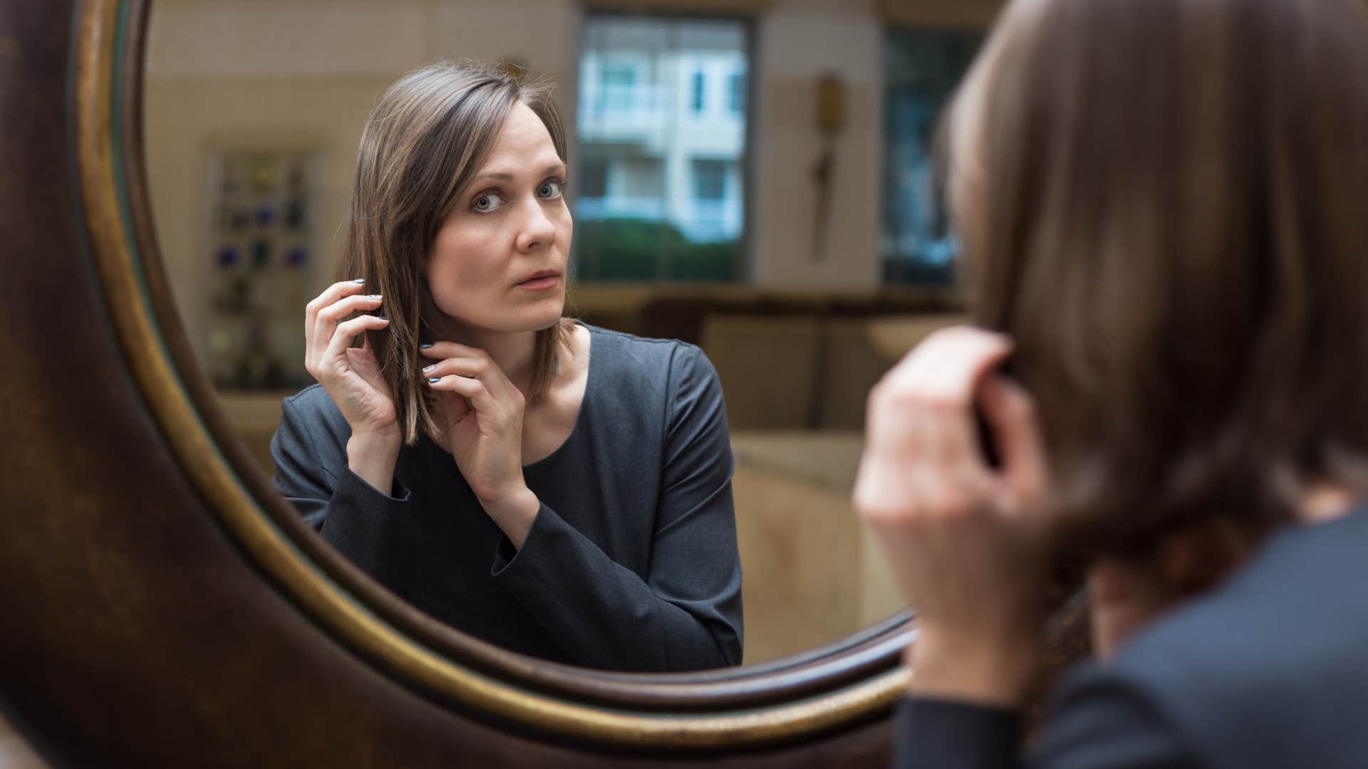 mirrors if you notice these things missing from someone's home they've probably been through a lot in life woman looking in mirror looking confused