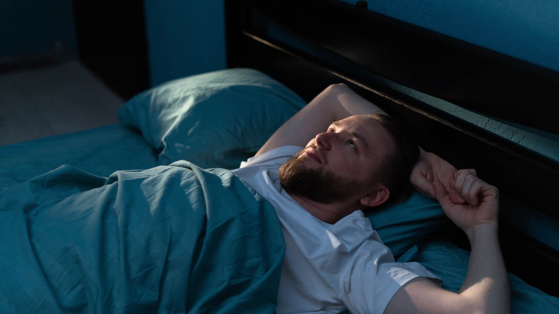 man in white shirt laying on bed as he replays their conversation in his head