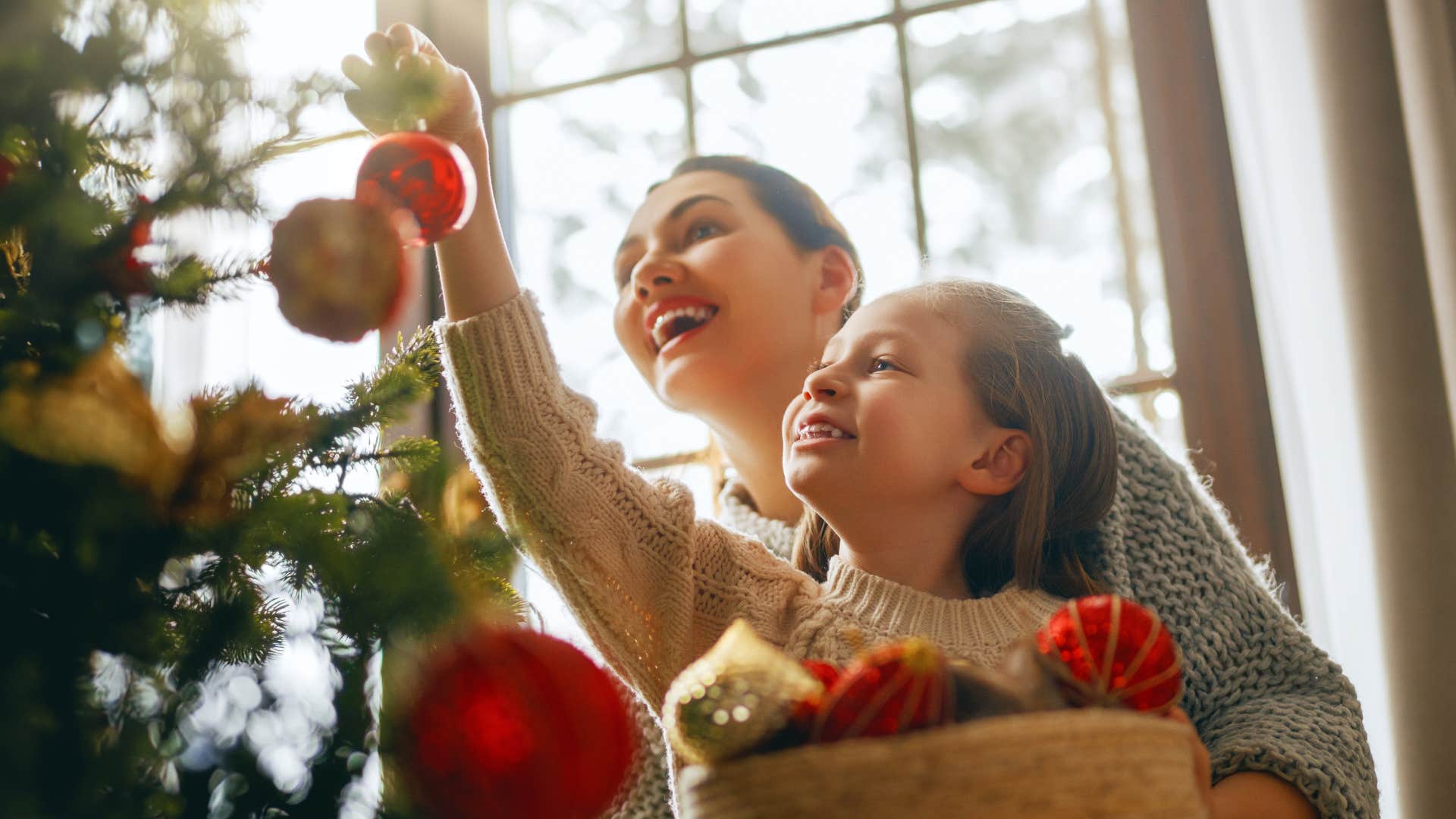 mom helping daughter decorate the christmas tree