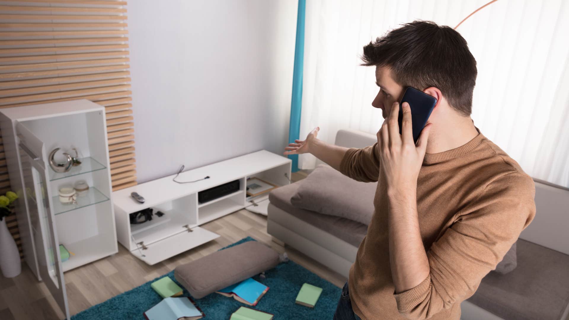 man on the phone looking at broken items in his house