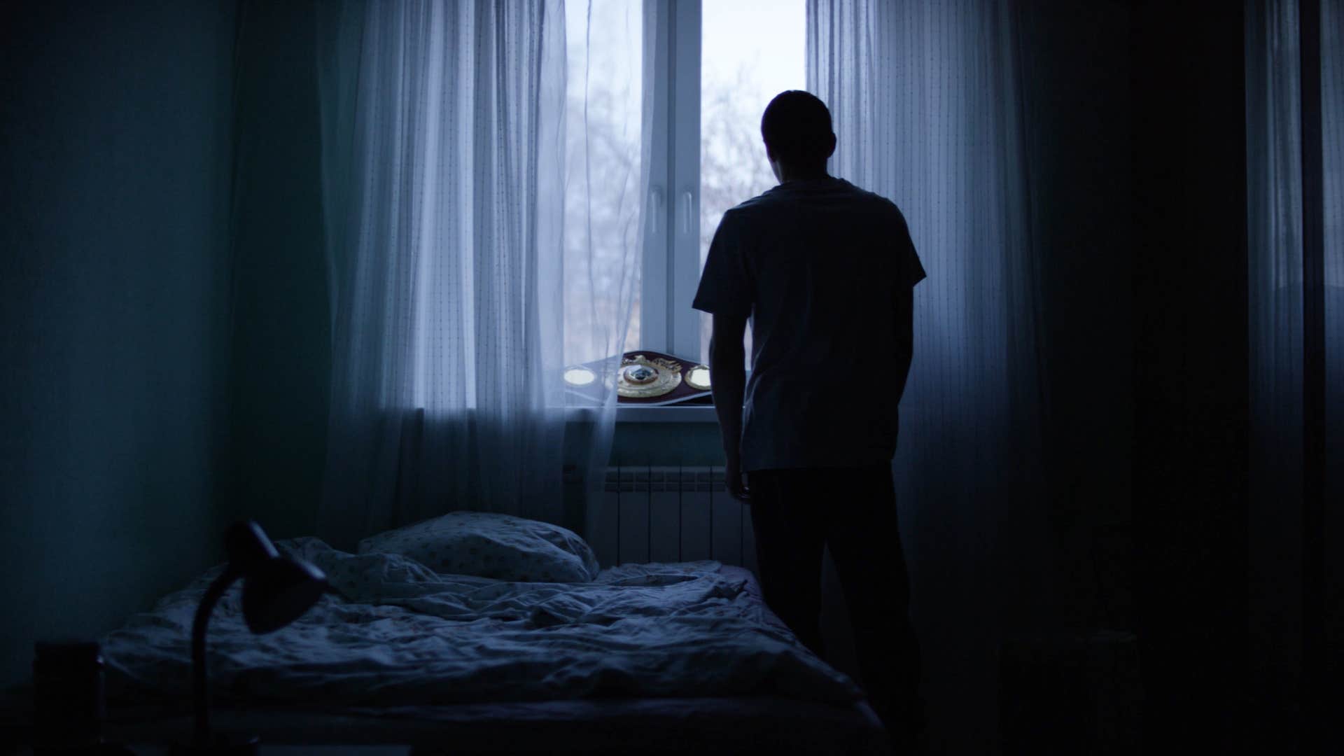 sad man in the dark standing in front of window