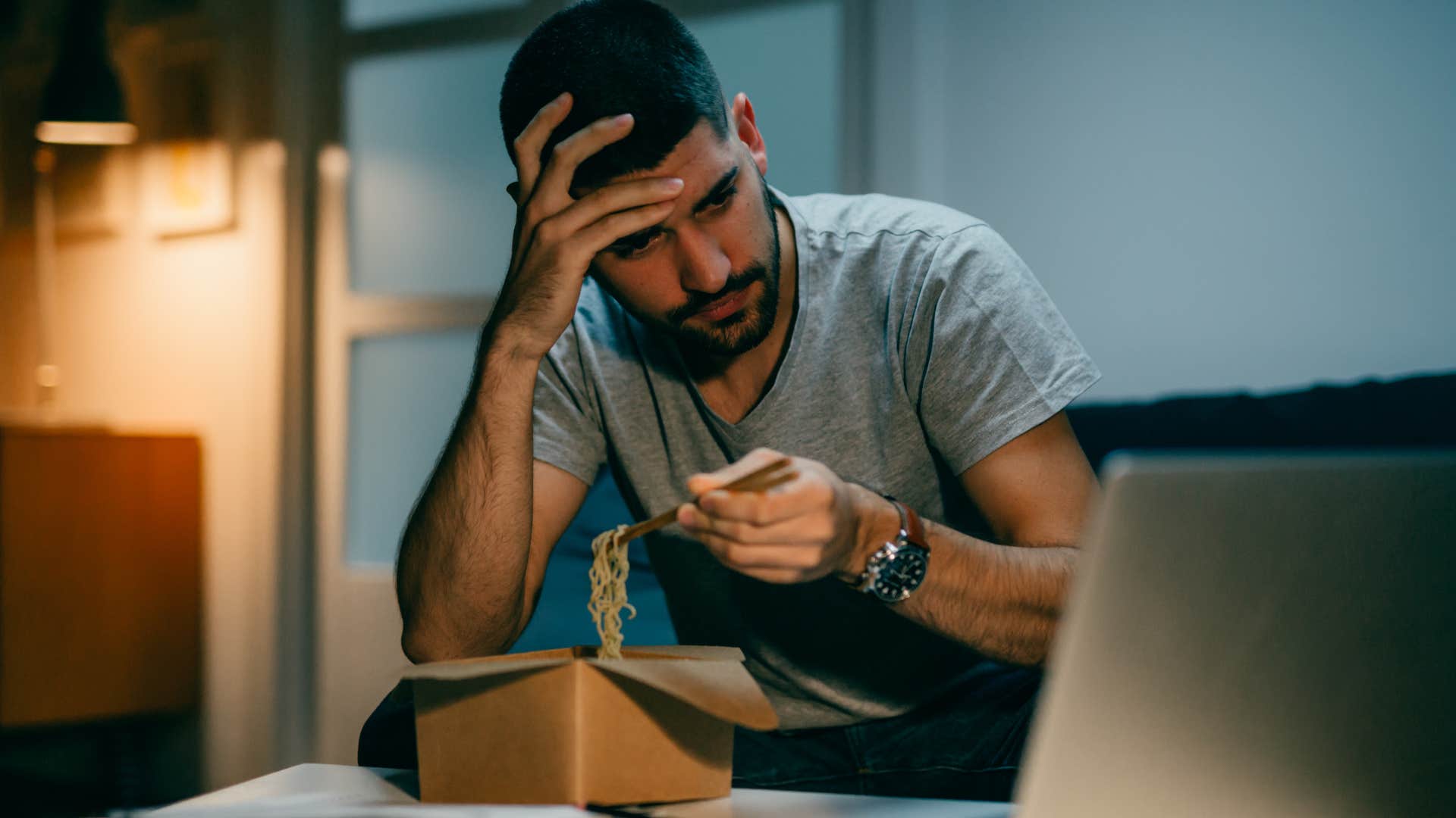 sad man eating fast food looking at laptop