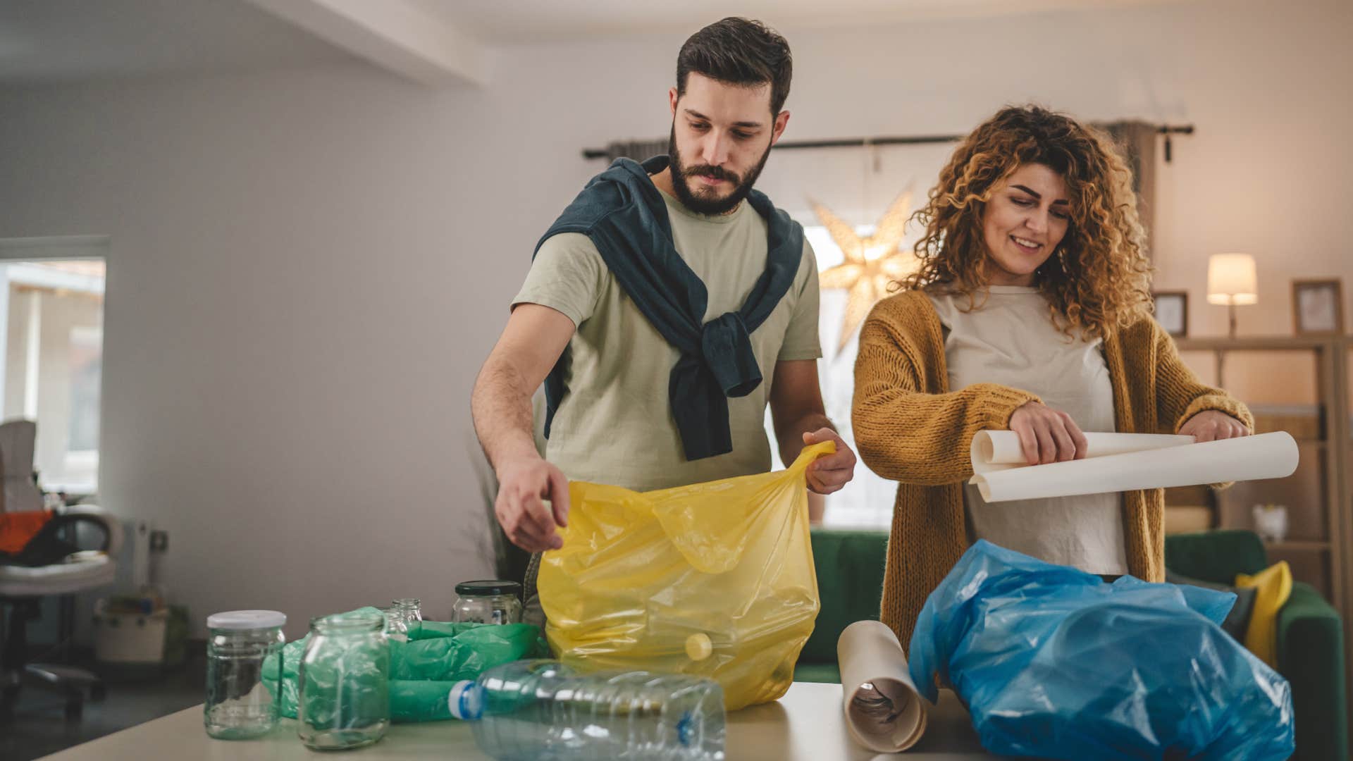 man looking at overflowing trash and recycling with woman