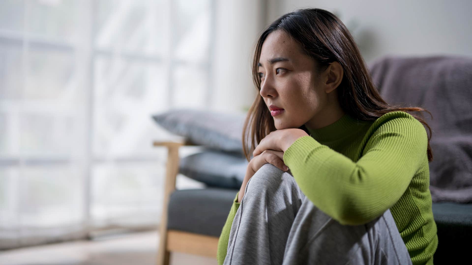 woman in green shirt criticizes themselves more as she thinks while sitting on the ground