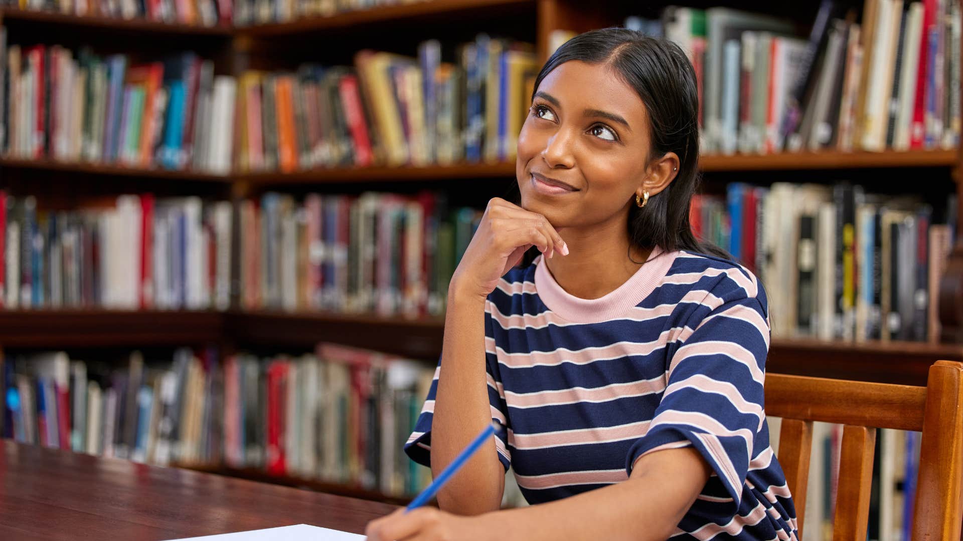 woman in stripped shirt daydreaming as she's at library 