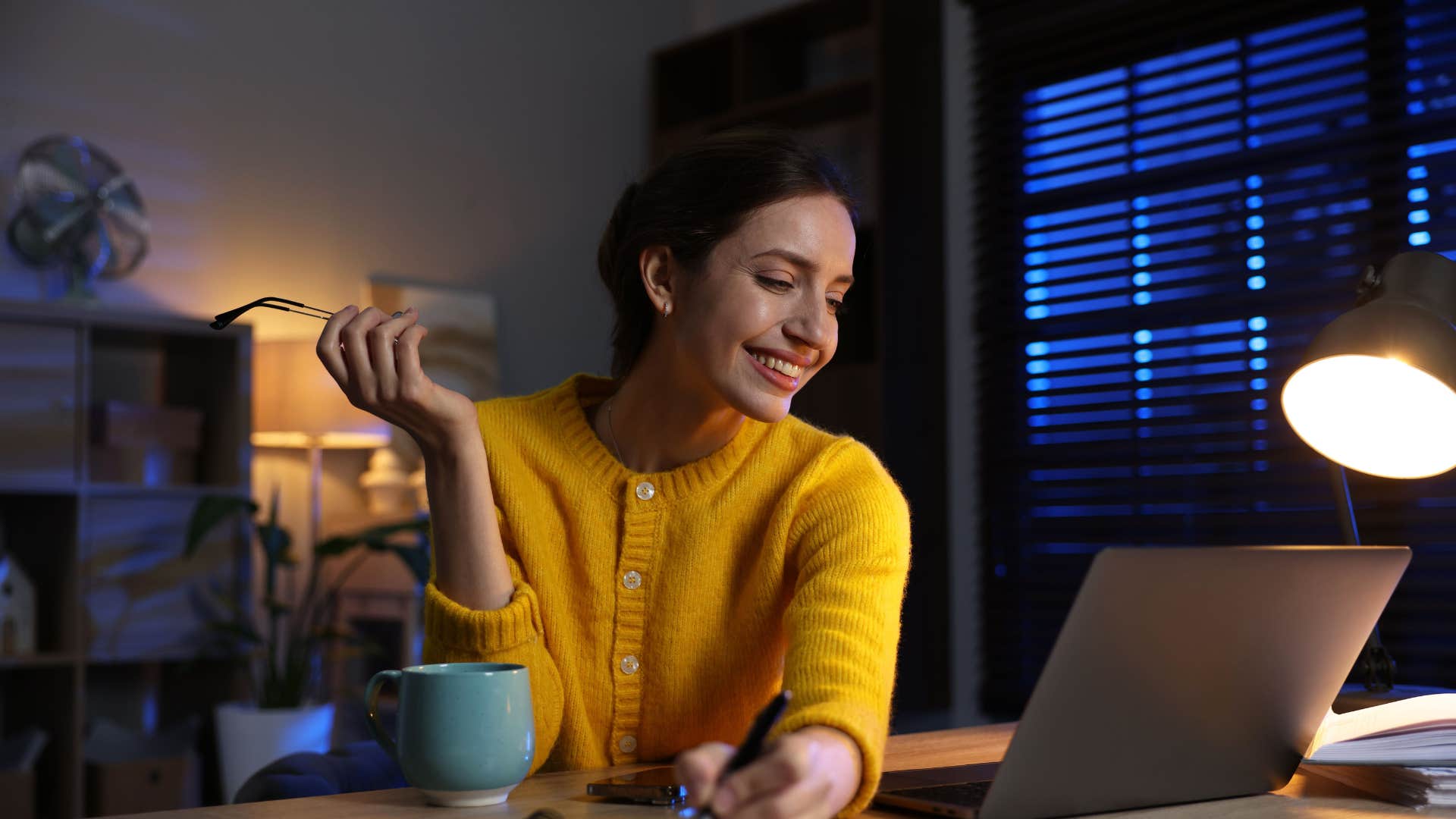 woman in yellow shirt smiling as she has unusual sleep or work patterns so she's staying up late to work