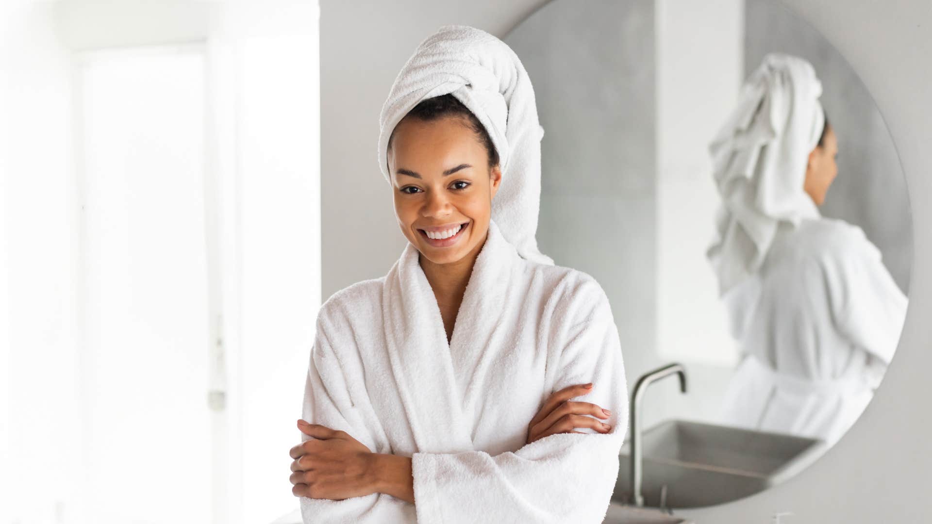 woman with white bathrobe about to take a cold shower as she smiles at camera and crosses arms