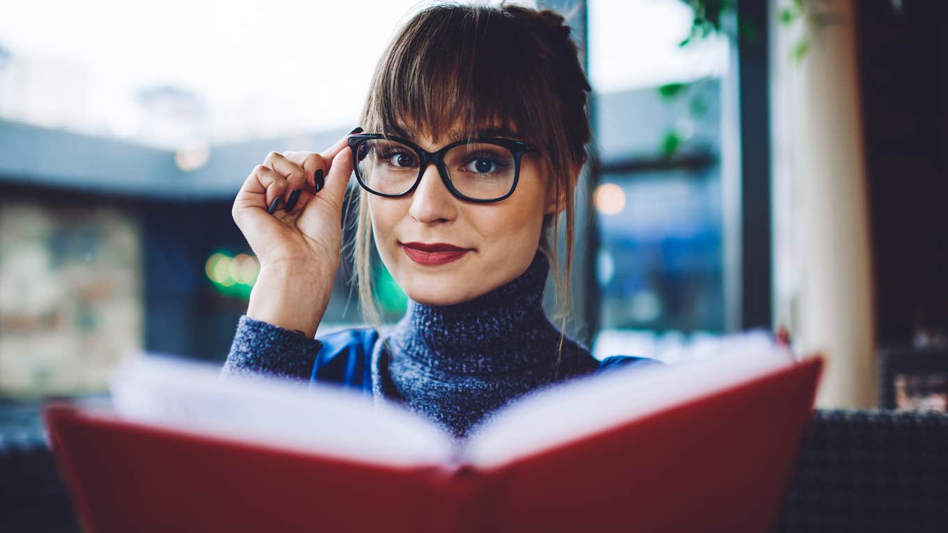 People Who Still Read Physical Books Instead Of Scrolling Usually Have These Rare Personality Traits intelligent woman reading a book holding her glasses