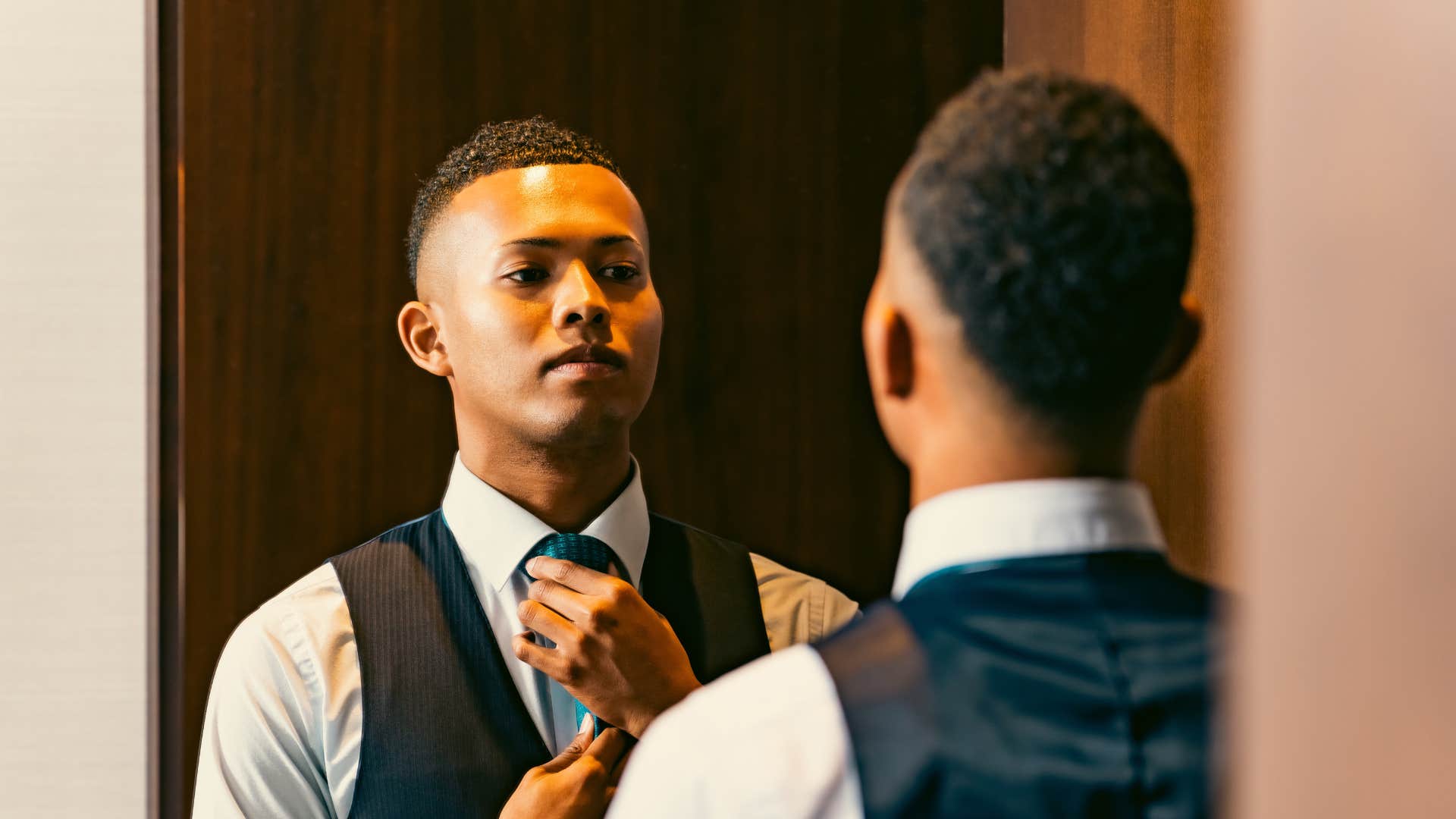 man adjusting tie in a full length mirror