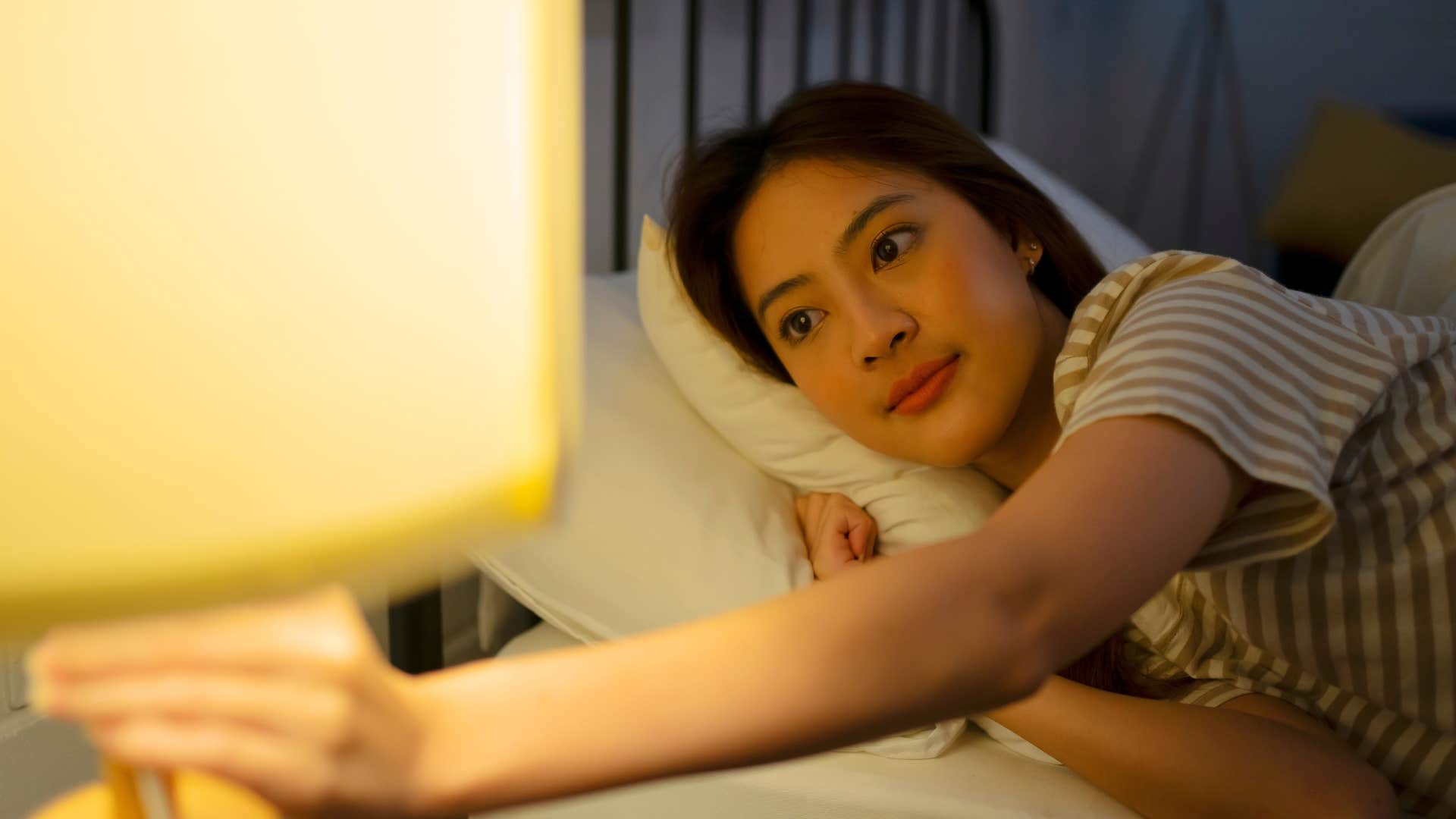 woman turning off the light in bed to regulate her temperature